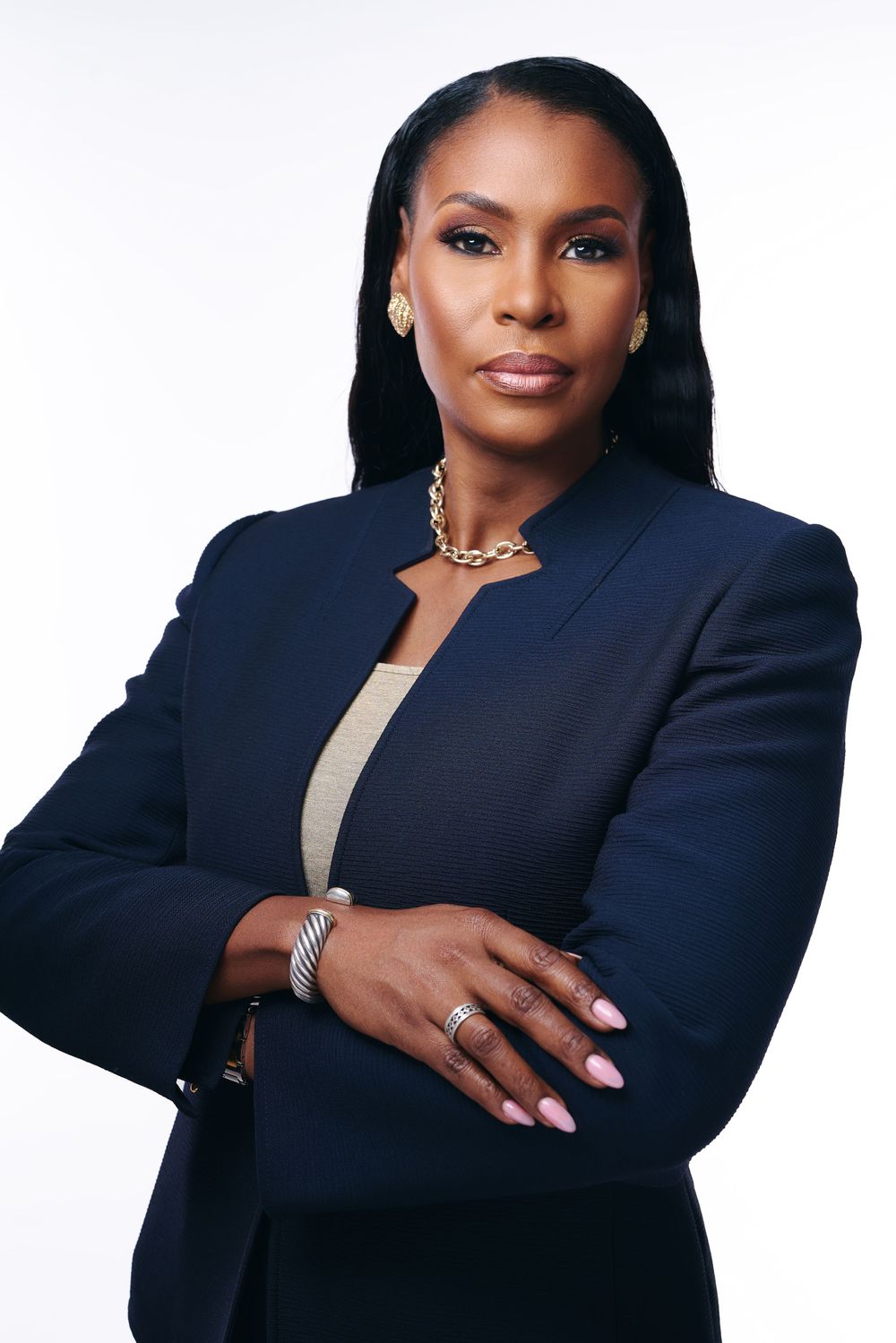 Professional portrait of woman in navy blazer with statement necklace against white background.