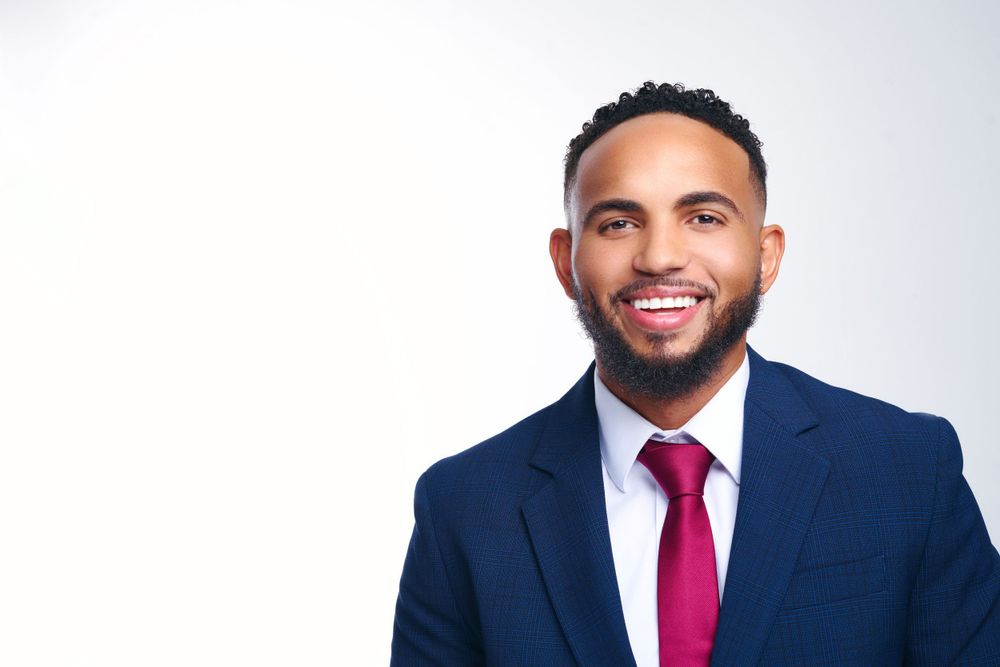 Professional headshot of a man in navy suit and red tie smiling against white background.