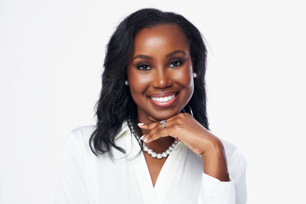 Professional headshot of woman in white blouse with pearl necklace against white background.