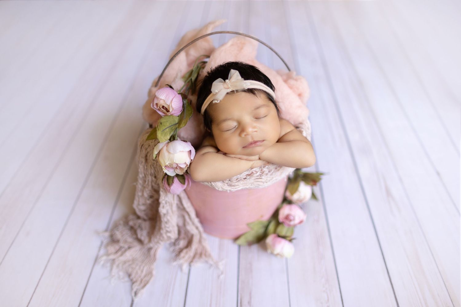 Newborn photography featuring soft pink decorations and floral elements on white wooden backdrop.