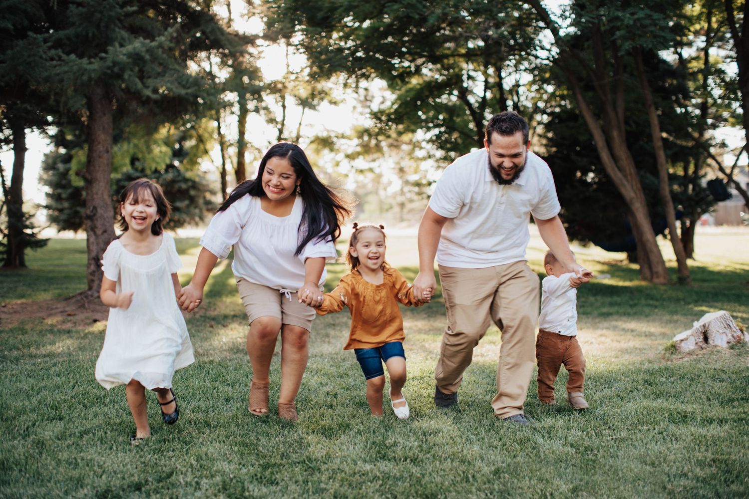 Tucson family photography capturing parents and children running together through a grassy park at sunset.