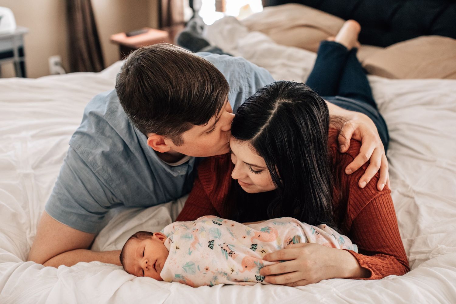 Tucson newborn family portrait of parents lying on the bed kissing their baby during a lifestyle session.