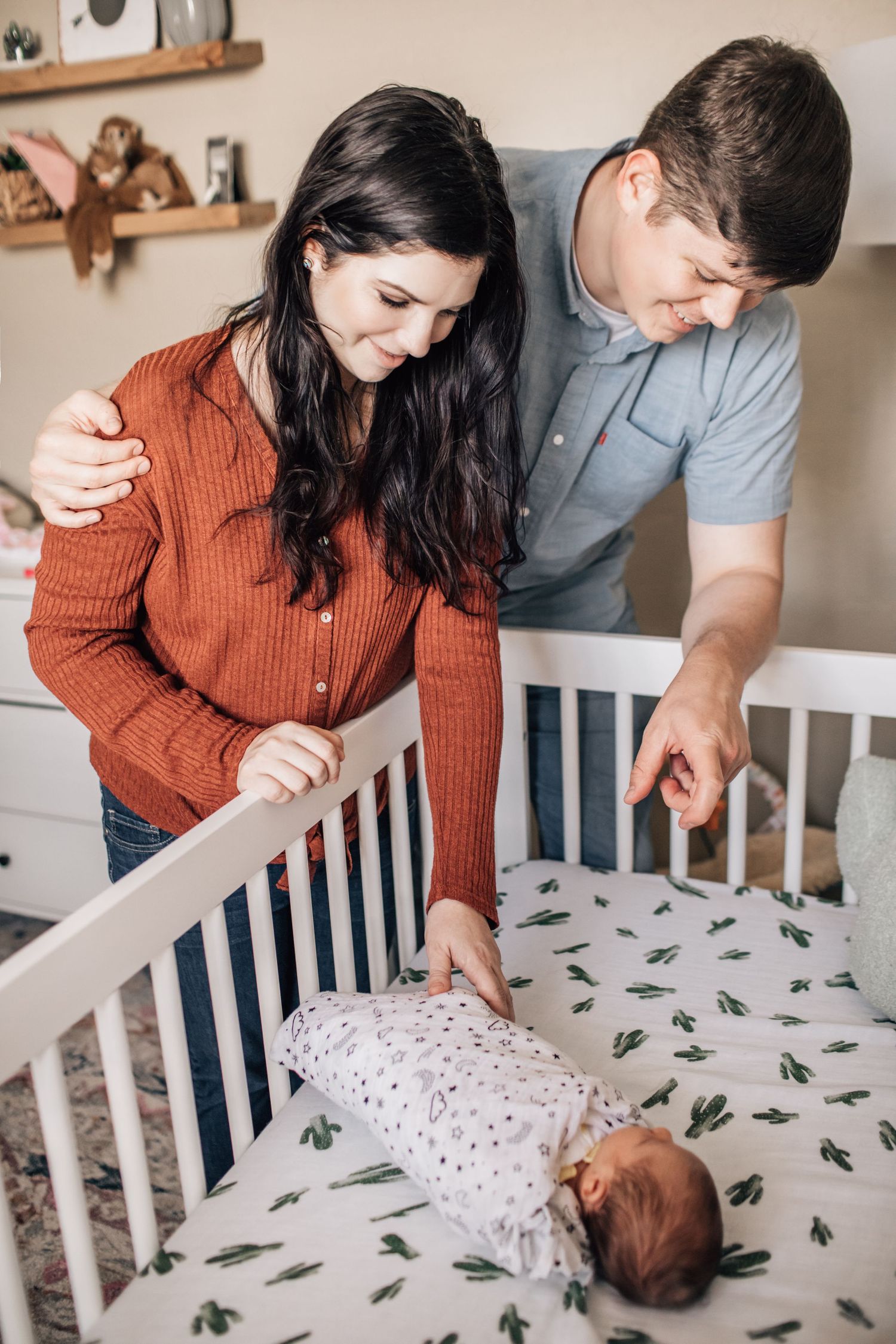 Tucson newborn lifestyle photo of parents leaning over the crib admiring their baby in a cozy nursery.