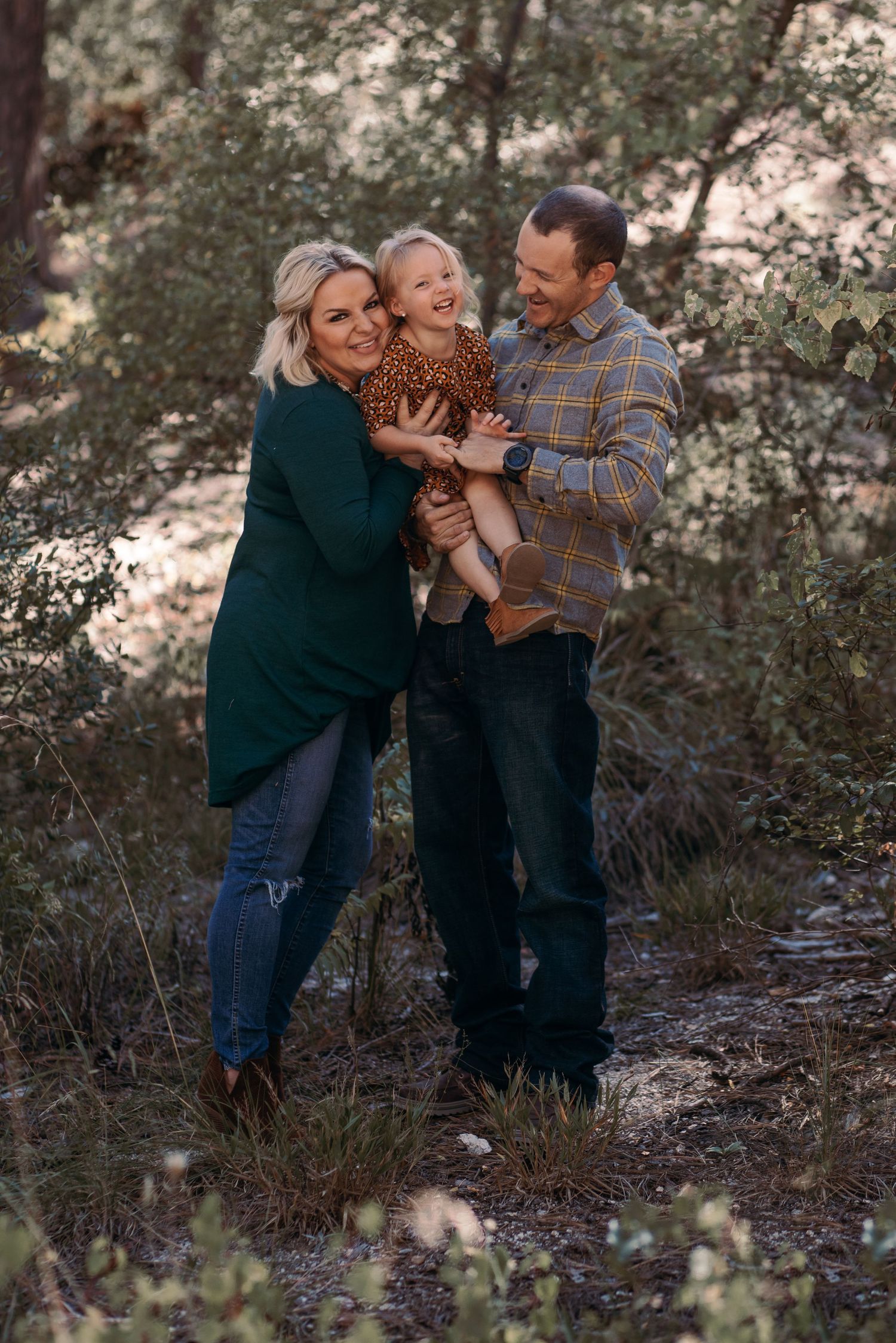 Tucson family photographer captures parents holding their toddler during a warm outdoor family session among desert trees.