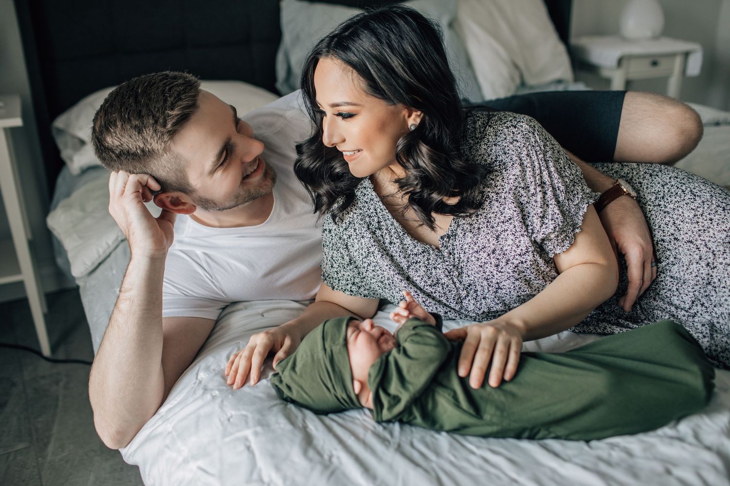 Tucson newborn lifestyle photo of parents lying on the bed cuddling their baby in a cozy home setting.