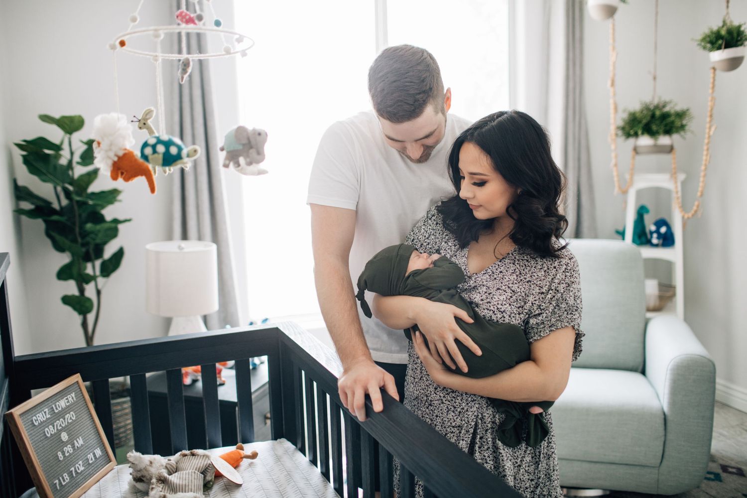 Tucson newborn photography of parents standing beside the crib lovingly watching their baby in a bright nursery.
