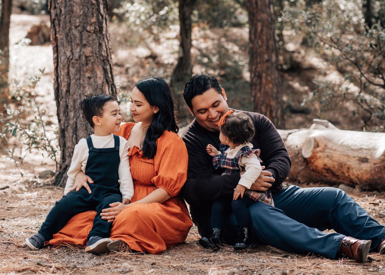 Tucson family photography capturing parents and kids laughing together on the forest floor in natural, candid moments in Mt. Lemmon.