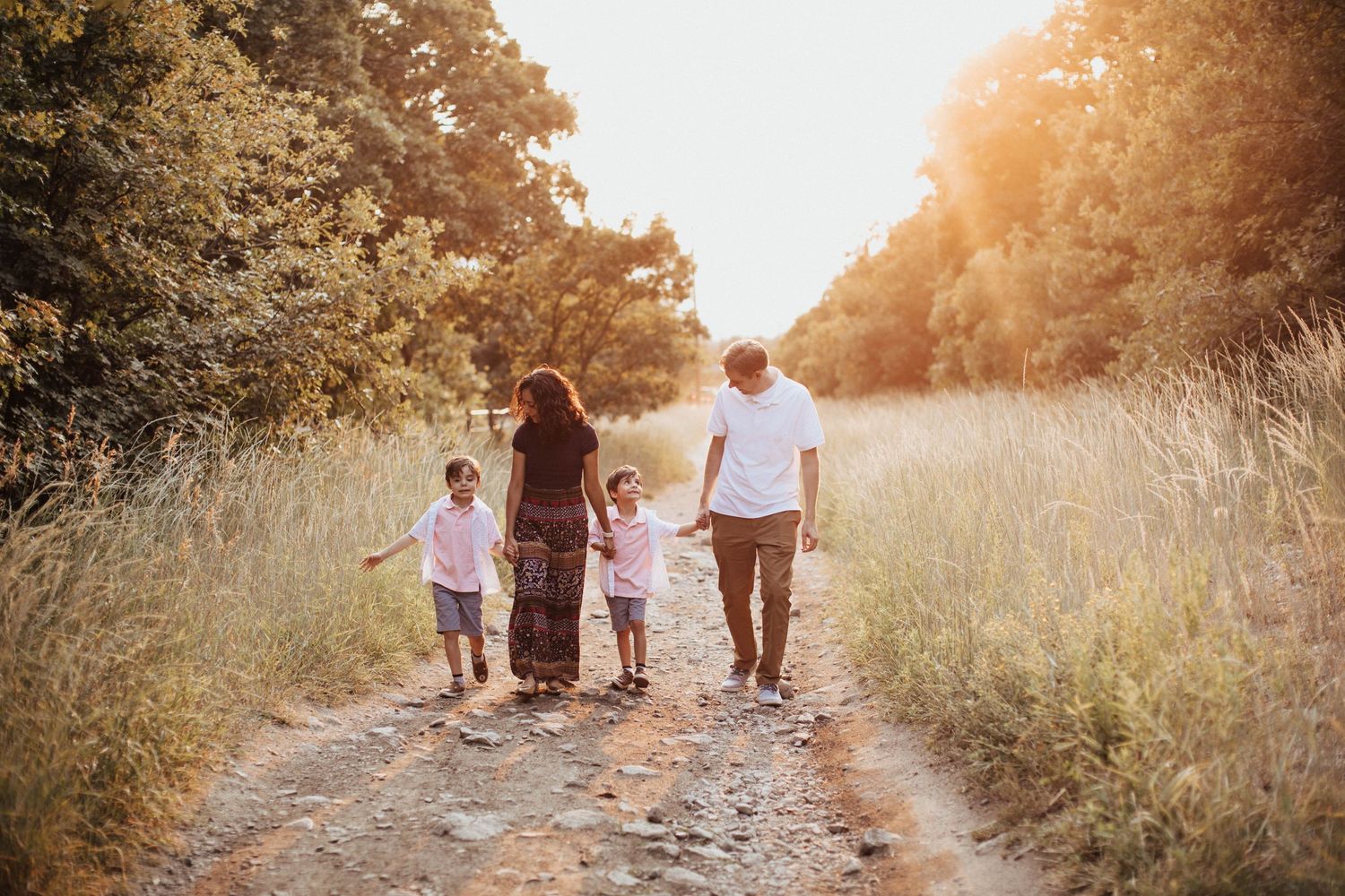 Tucson family photo of parents and children walking down a dirt path at sunset surrounded by tall grass and golden light.