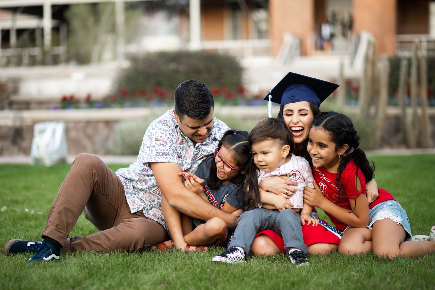 Tucson graduation photo of a University of Arizona senior celebrating in the grass with her family and children.