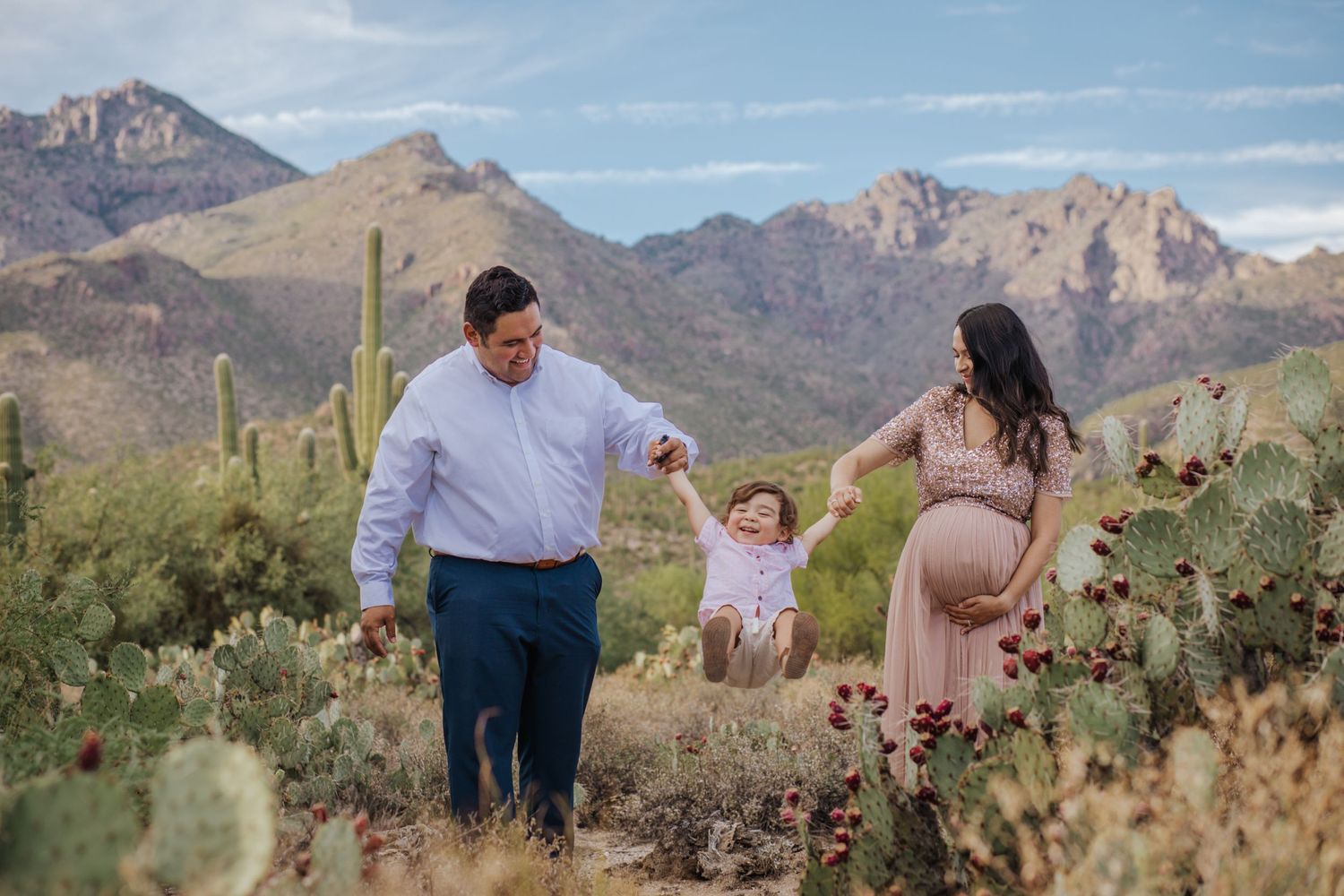 Tucson maternity photography featuring expecting parents walking together in the desert with the Catalina Mountains in the background.