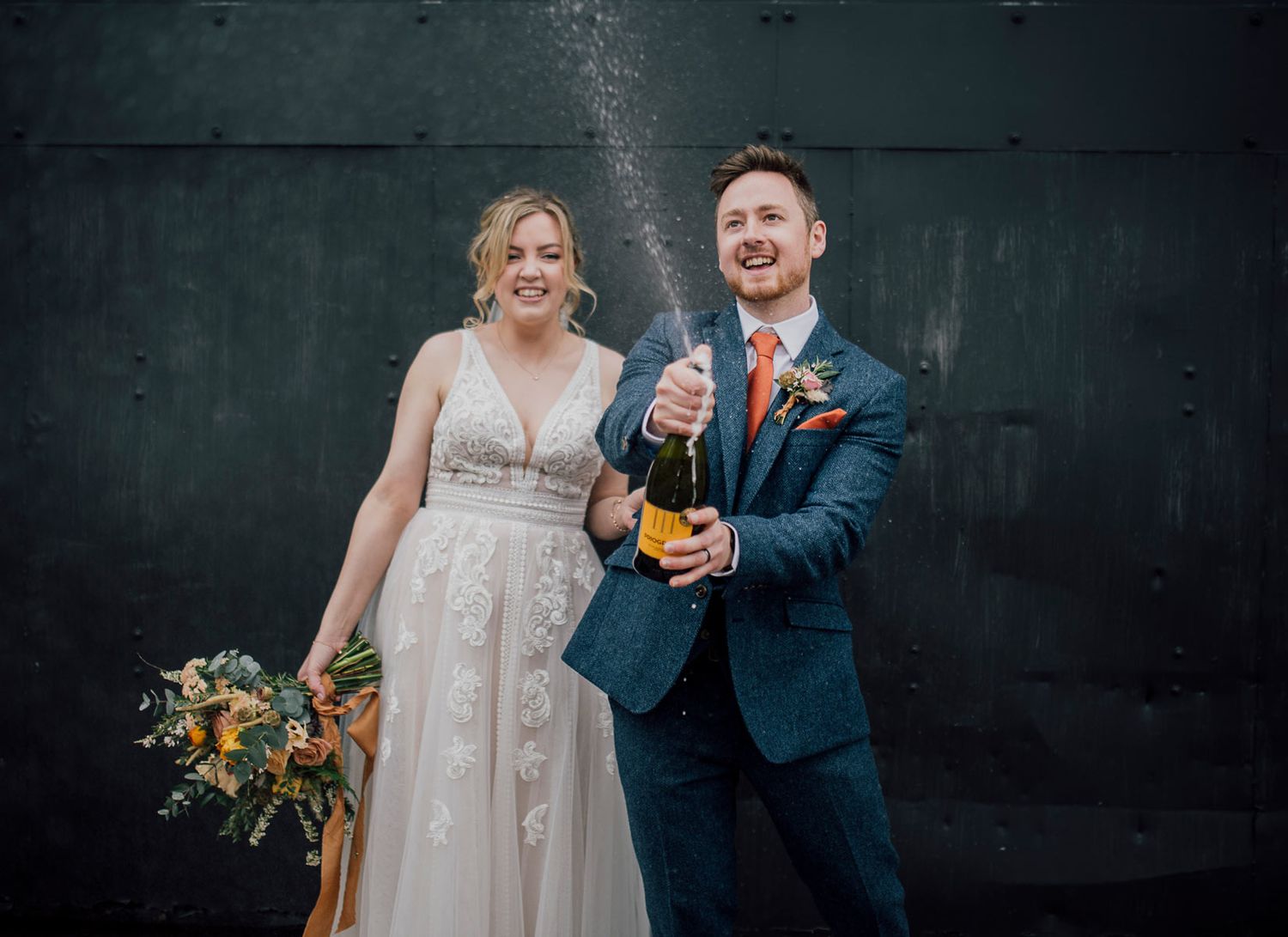 Wedding couple poses against dark wall with dramatic lighting and floral bouquet. Worcestershire Wedding photographer.