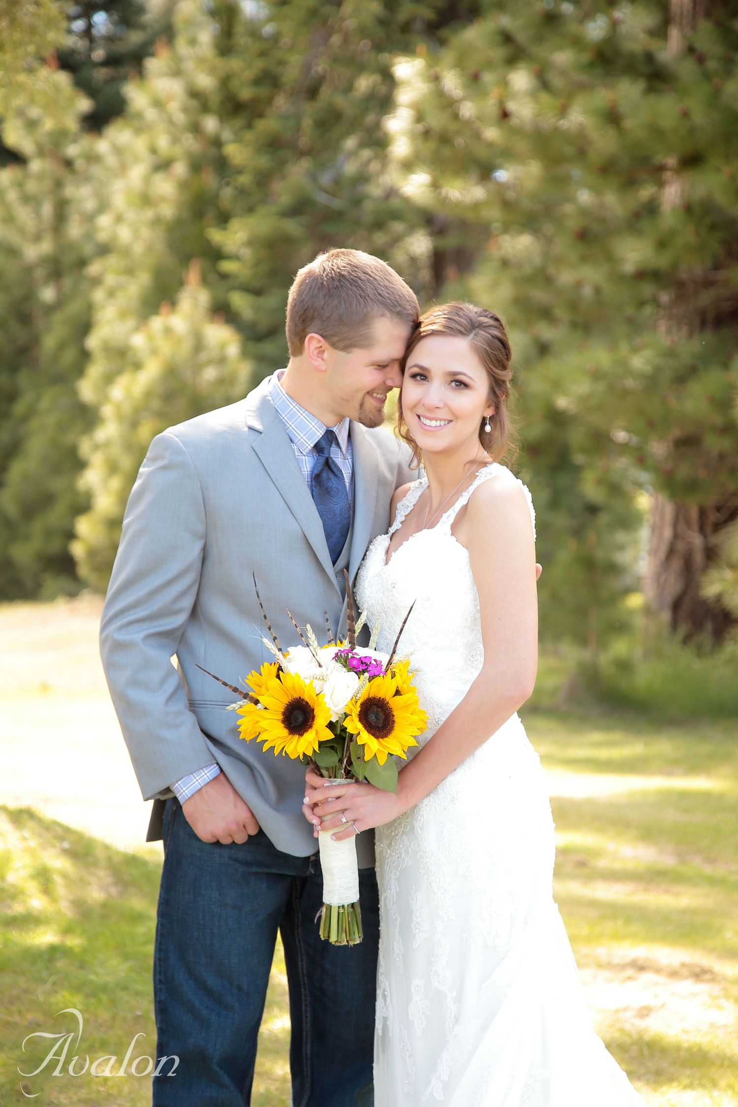 Wedding couple with sunflower bouquet sharing intimate moment in sunlit forest setting.