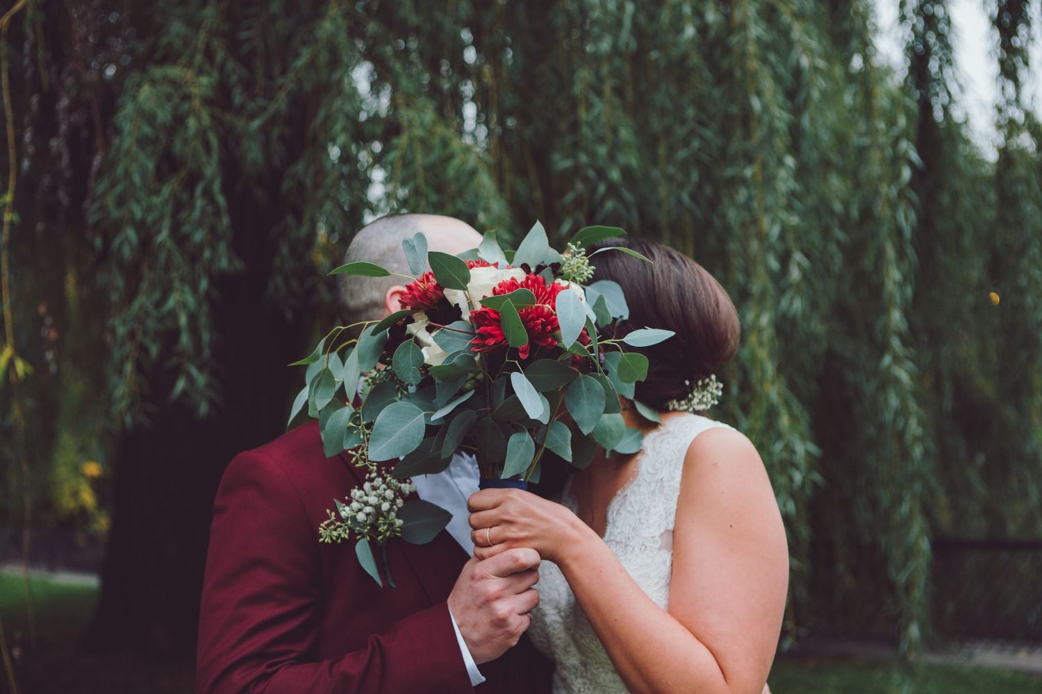 Wedding ceremony under weeping willow trees with floral arrangements.