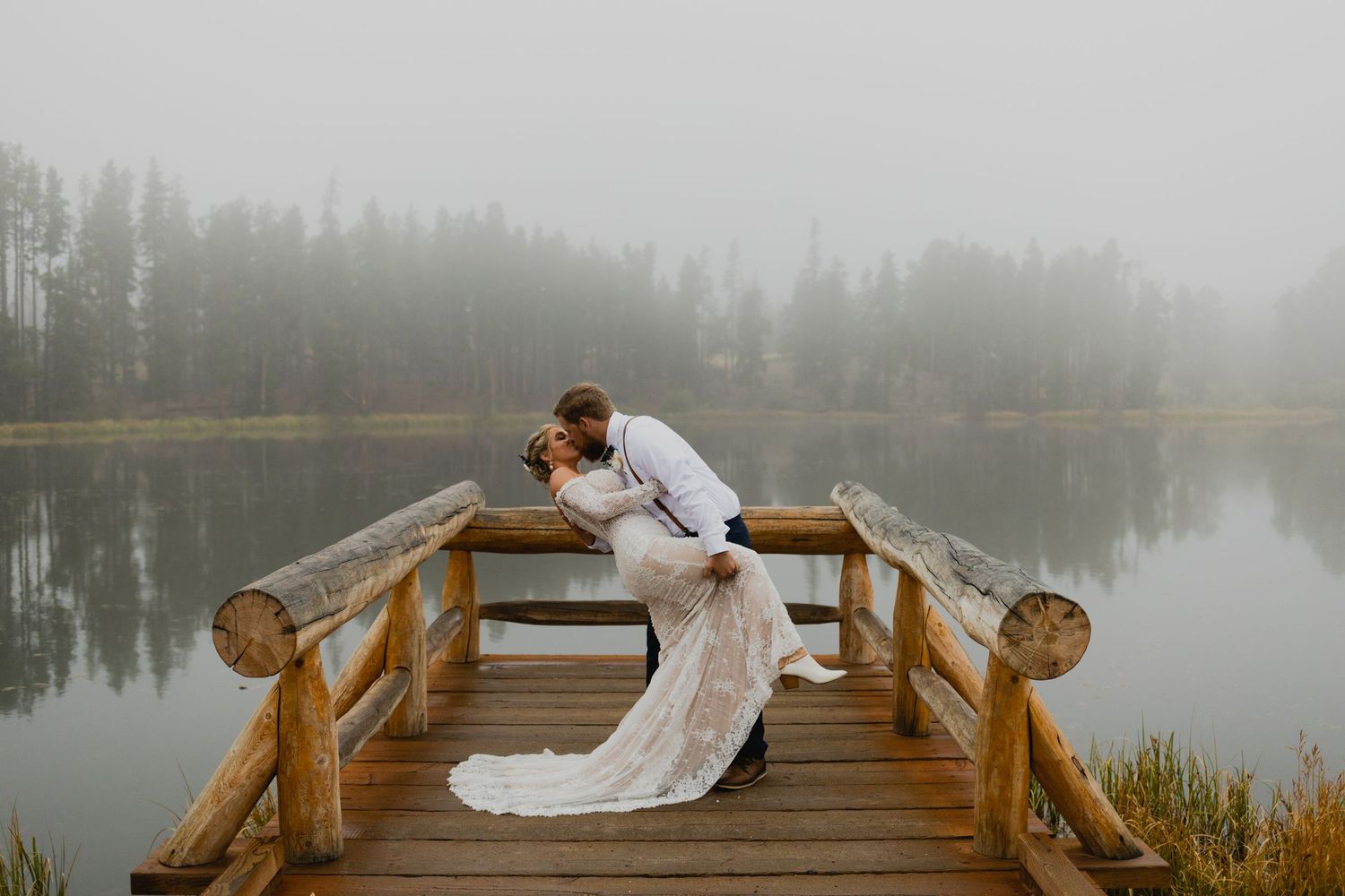 A couple shares an intimate moment on a wooden dock over a misty mountain lake.