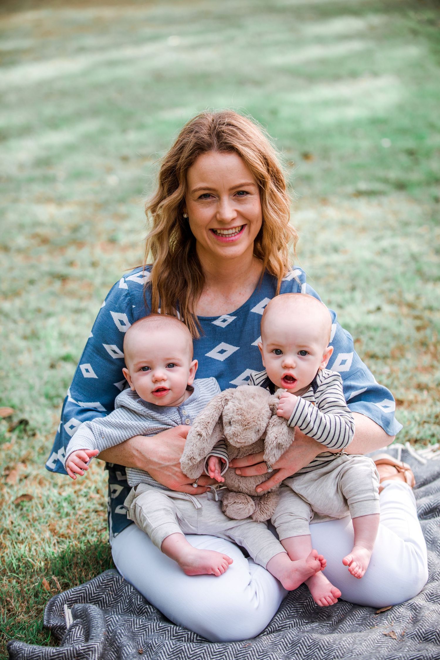A happy family moment with twin babies and parent sitting on a blanket in the grass.