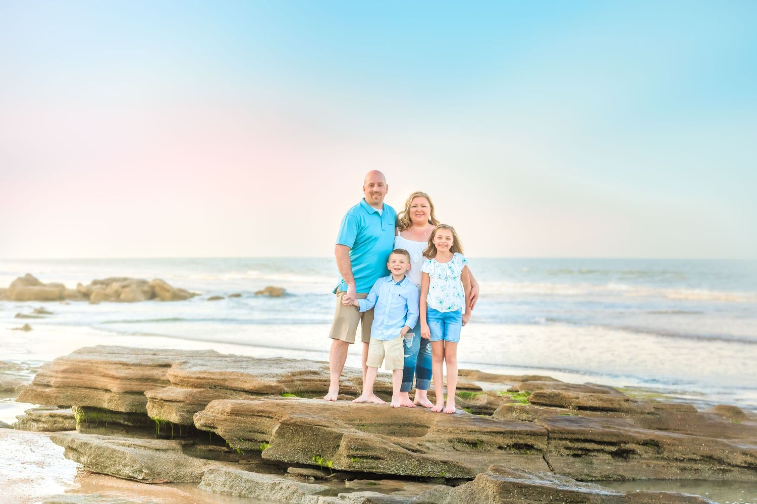 Family standing together on rocky coastal beach during sunset photoshoot.