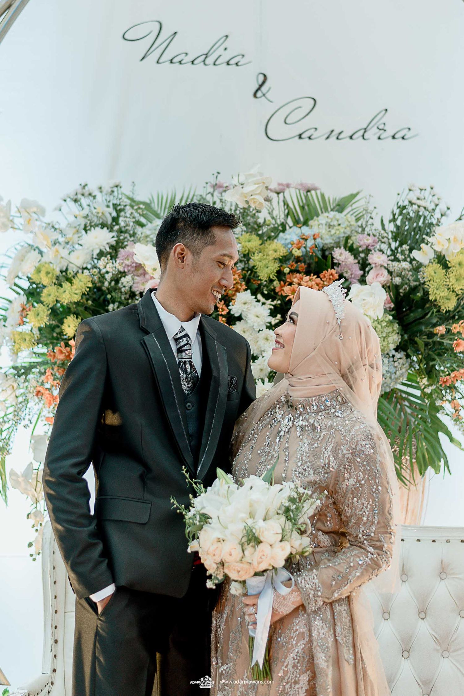 Elegant wedding portrait under decorative name signage with lush floral arrangements.