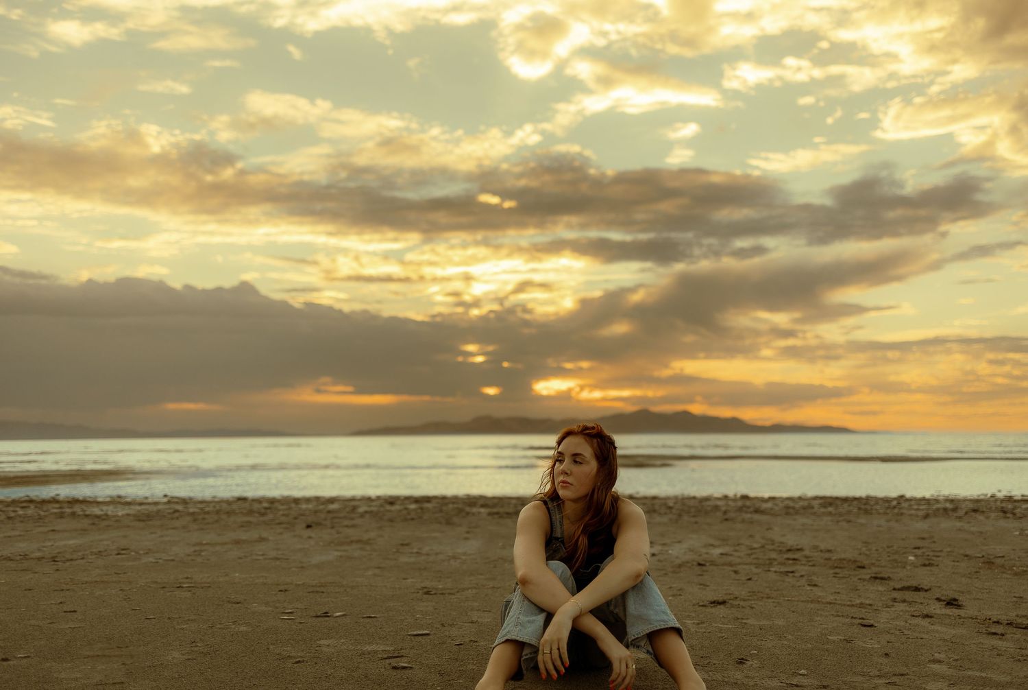 Girl staring into distance with lake and orange and yellow sunset behind her