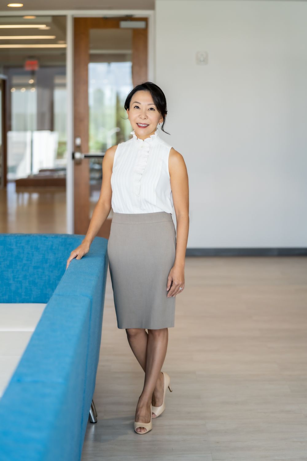 Professional wearing white sleeveless top and gray skirt in modern office space.