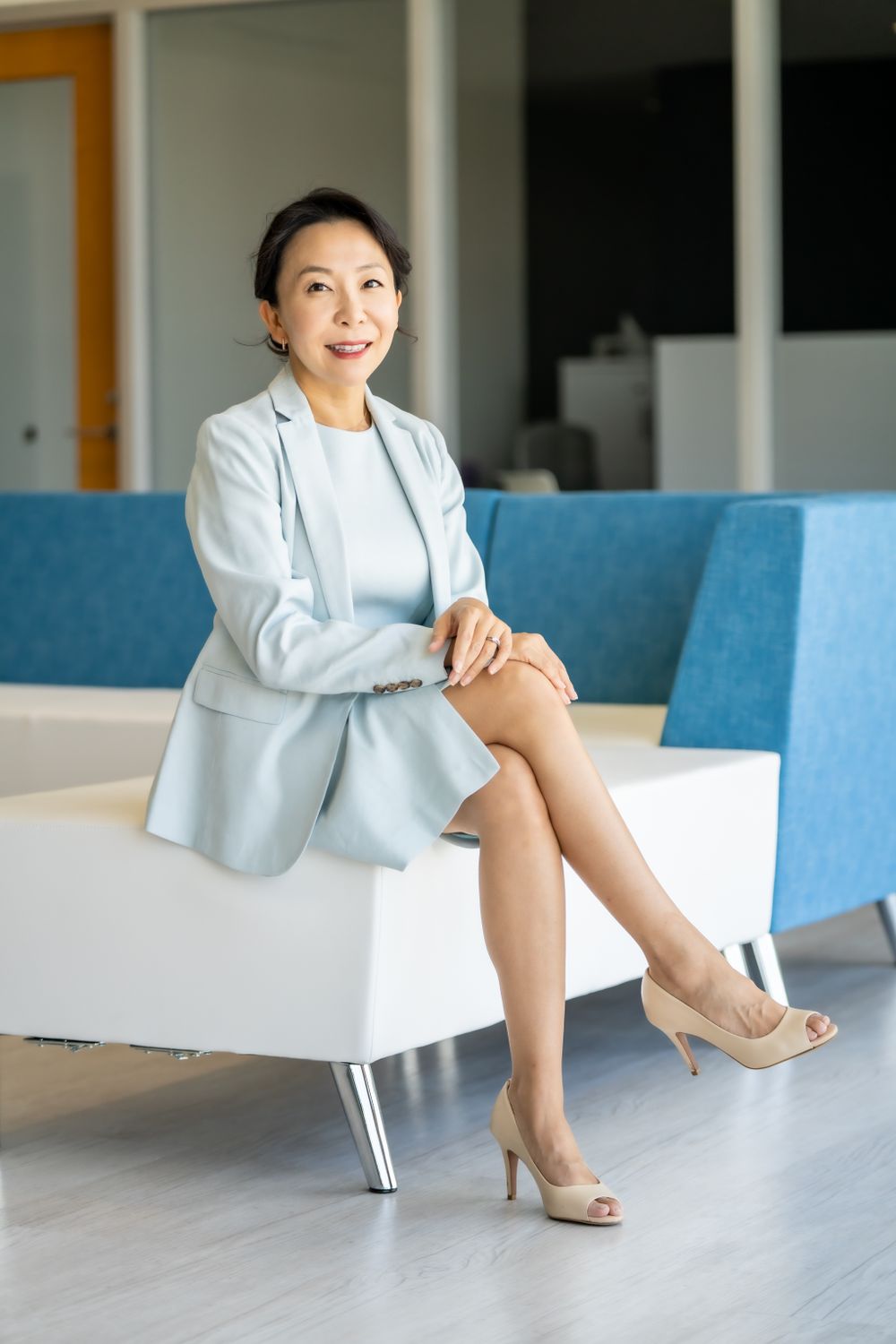 Professional in light blue blazer sitting elegantly on white modern office furniture.