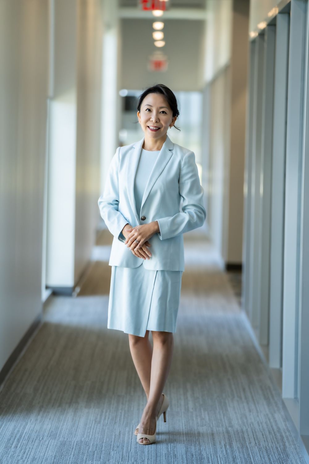 Professional in light blue suit walking confidently down office hallway.