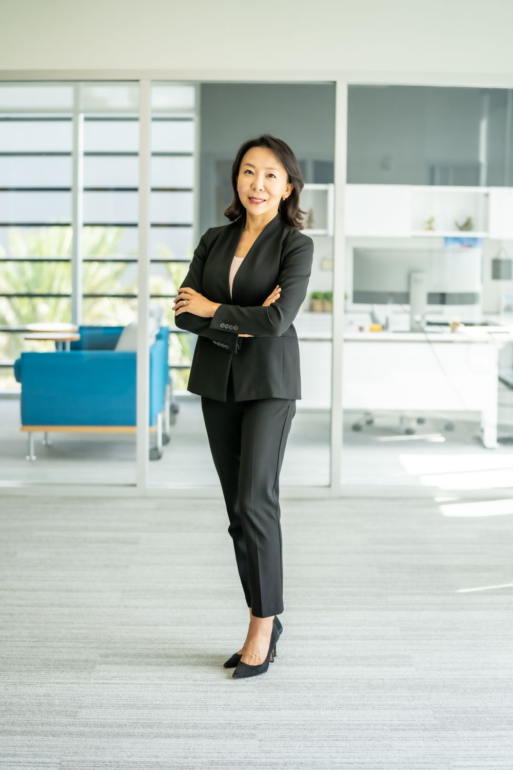 Professional wearing a black business suit stands confidently in a modern office setting.