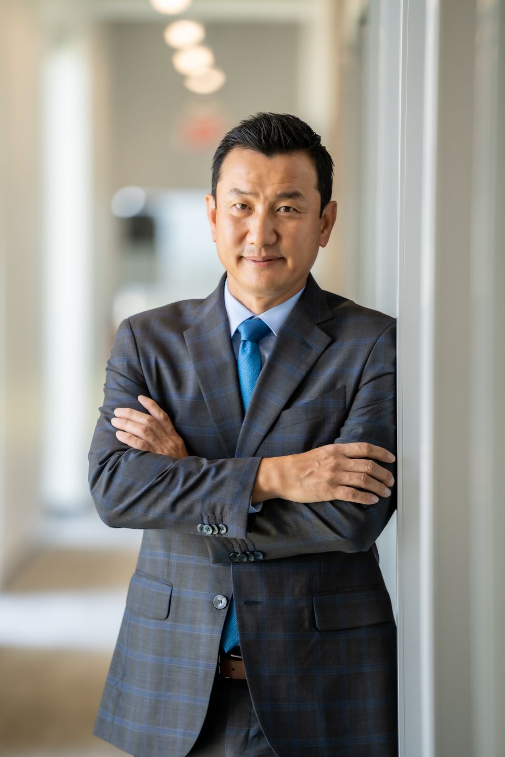 Professional in a gray suit and blue tie stands against an office hallway background.