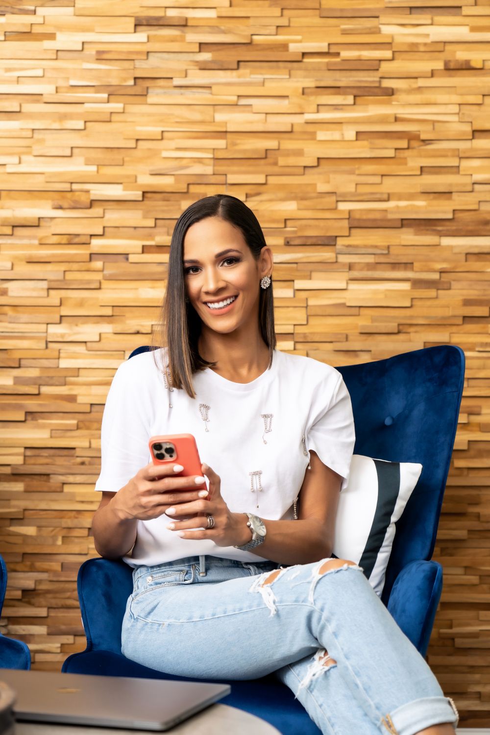 Casual lifestyle photo with woman using phone while relaxing in blue velvet chair.
