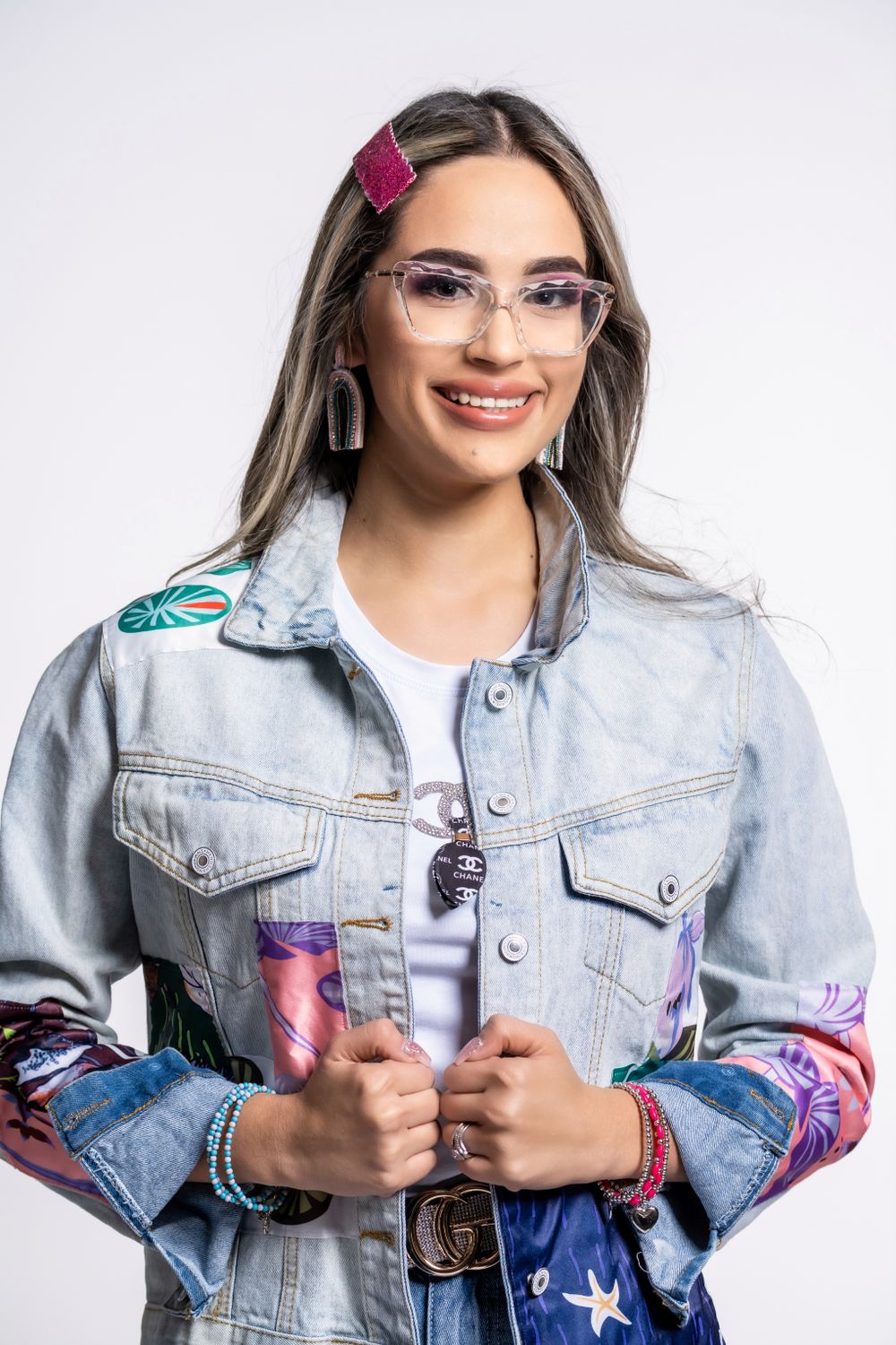 Studio portrait of a person wearing glasses and denim jacket with decorative patches.