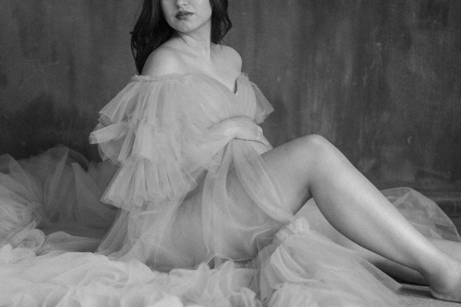 Maternity photography session in a studio in Richardson Texas. Woman holding pregnant belly with luxurious dress on.
