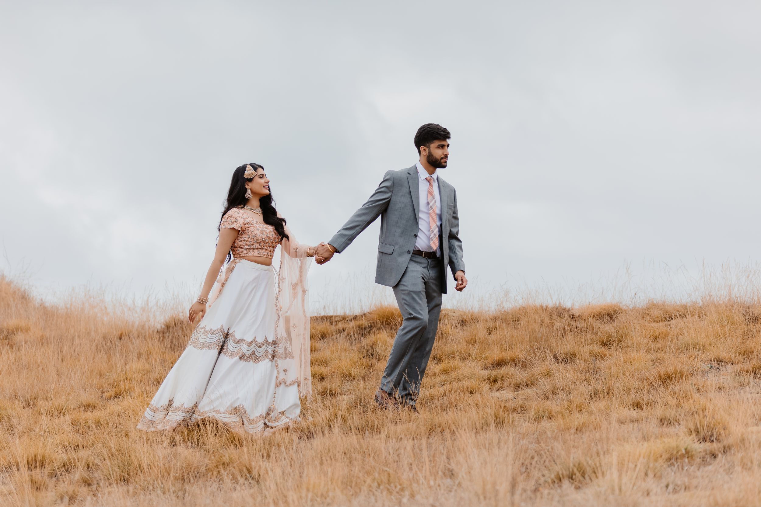A couple in wedding attire walking together on a golden hillside.