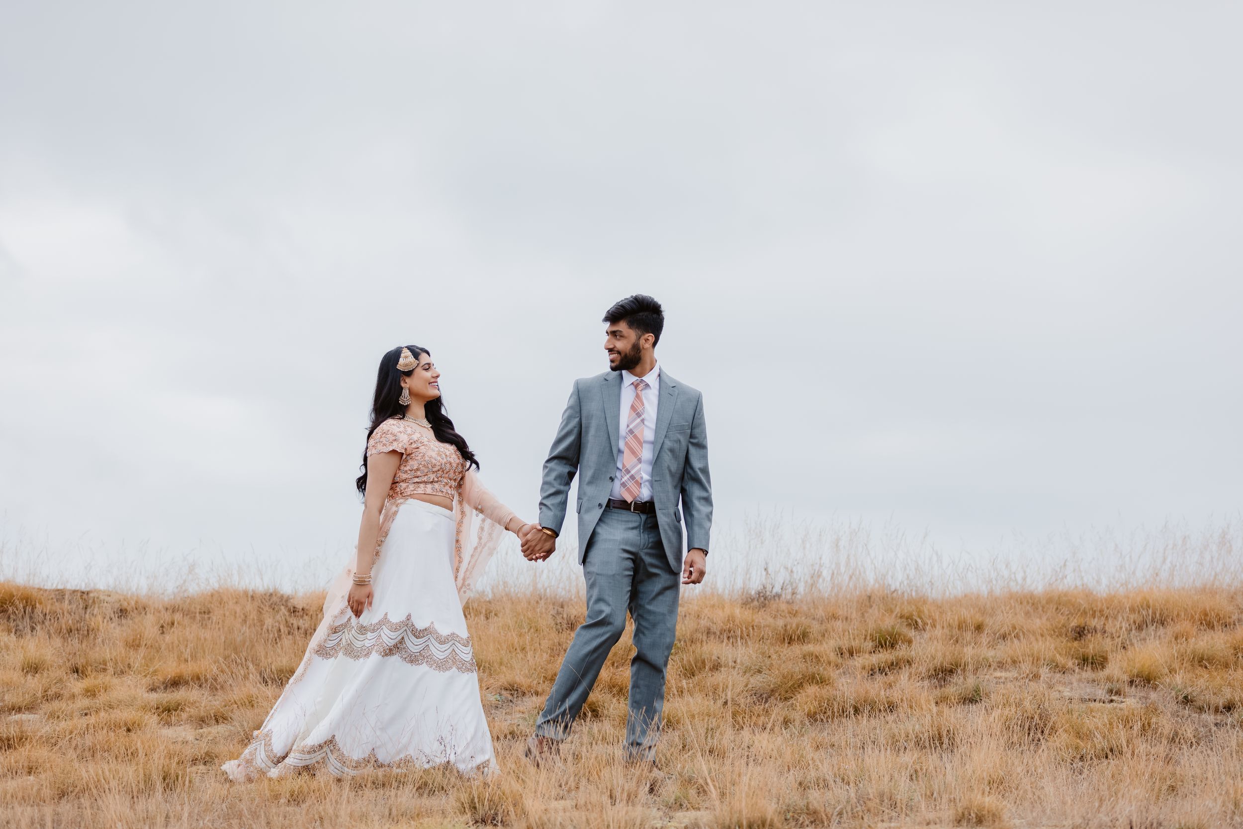 A couple in wedding attire sharing a joyful moment on a windswept hilltop.