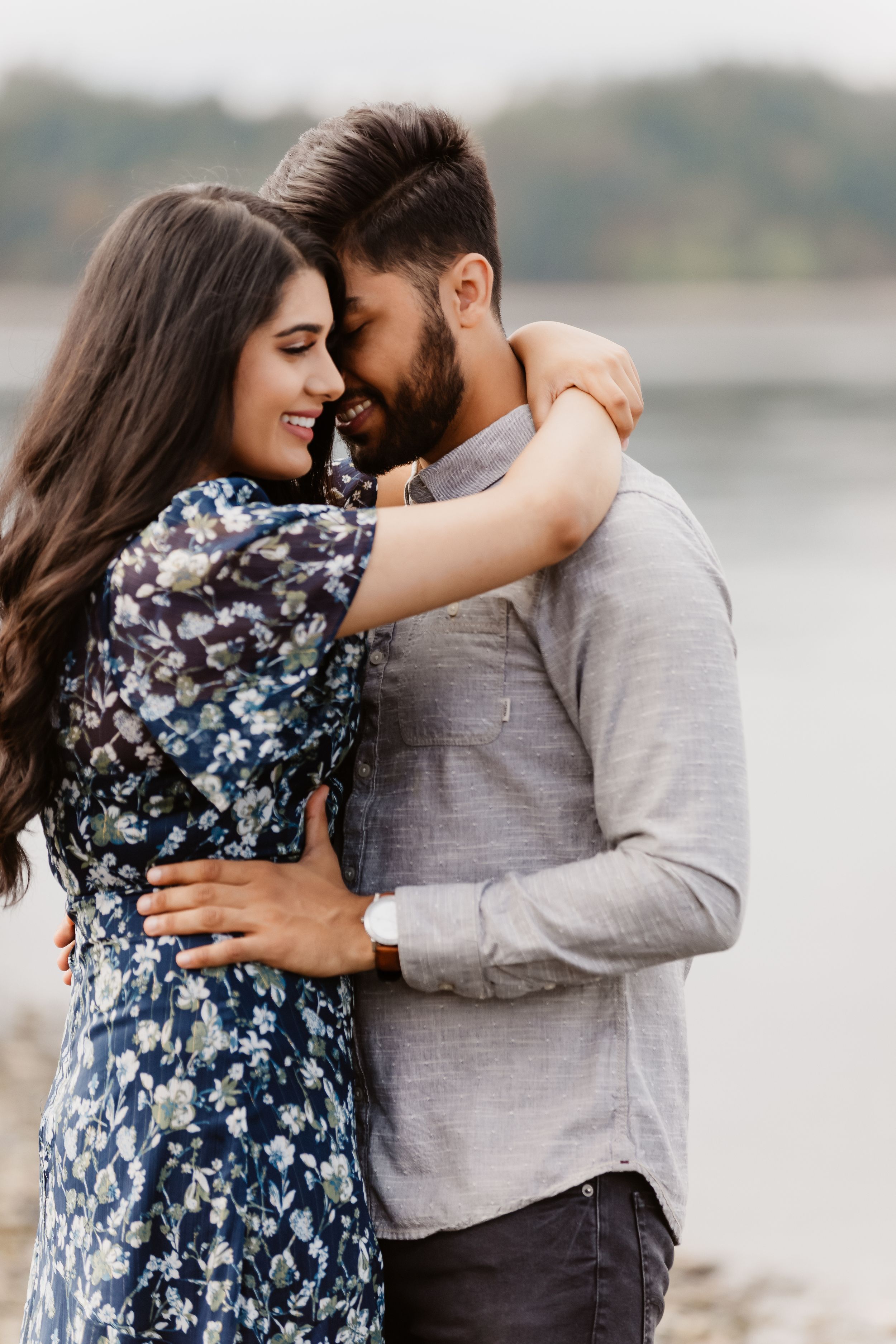 A romantic couple embraces by a lake, with the woman wearing a blue floral dress.
