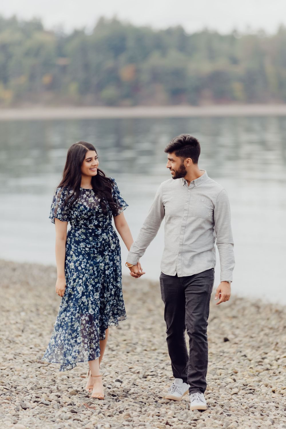 A couple holding hands while walking along a peaceful waterfront path.