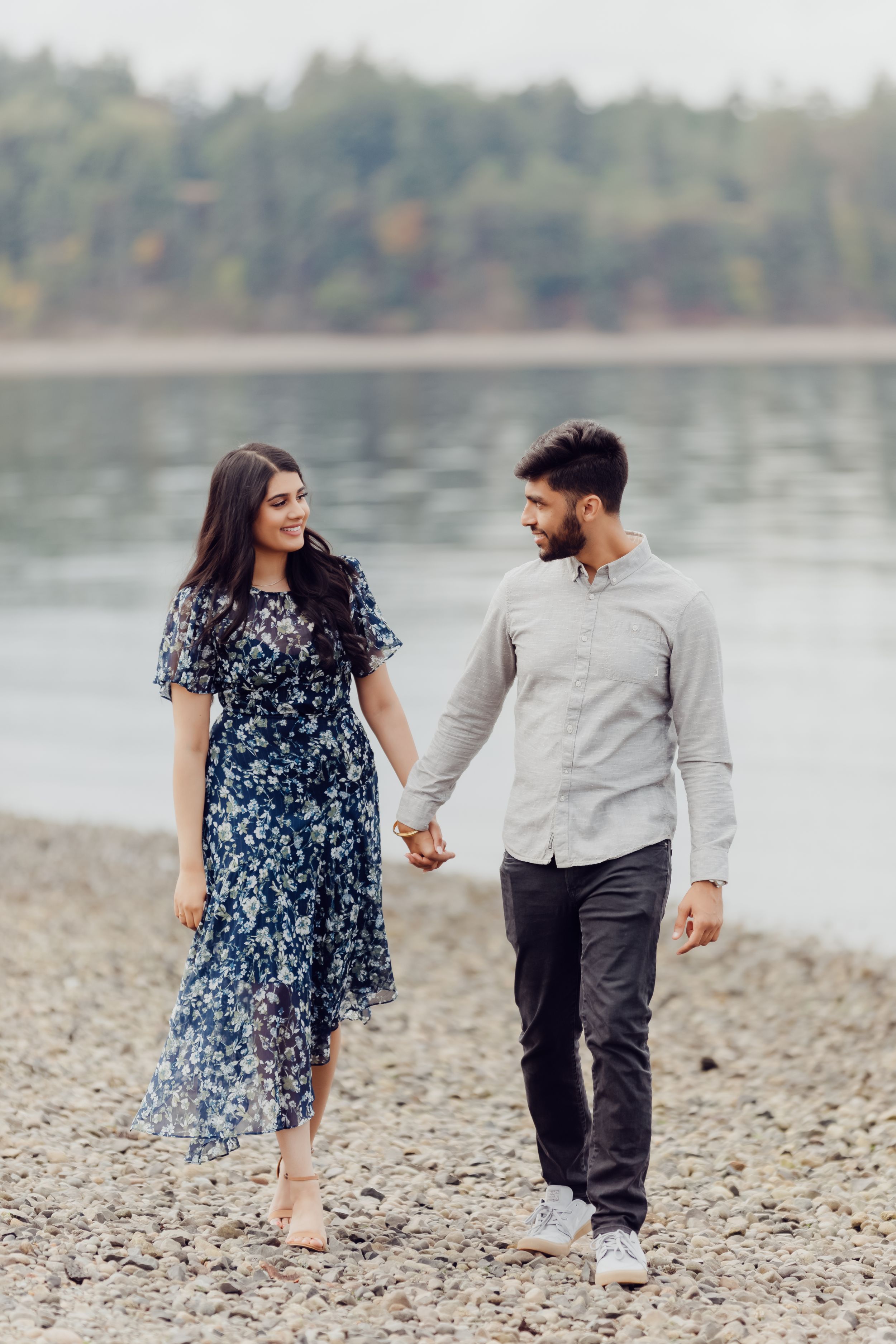 A couple holding hands while walking along a peaceful waterfront path.