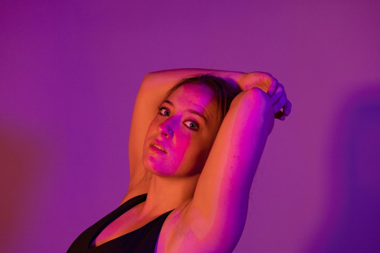 Athletic figure poses dramatically under magenta and purple studio lighting.