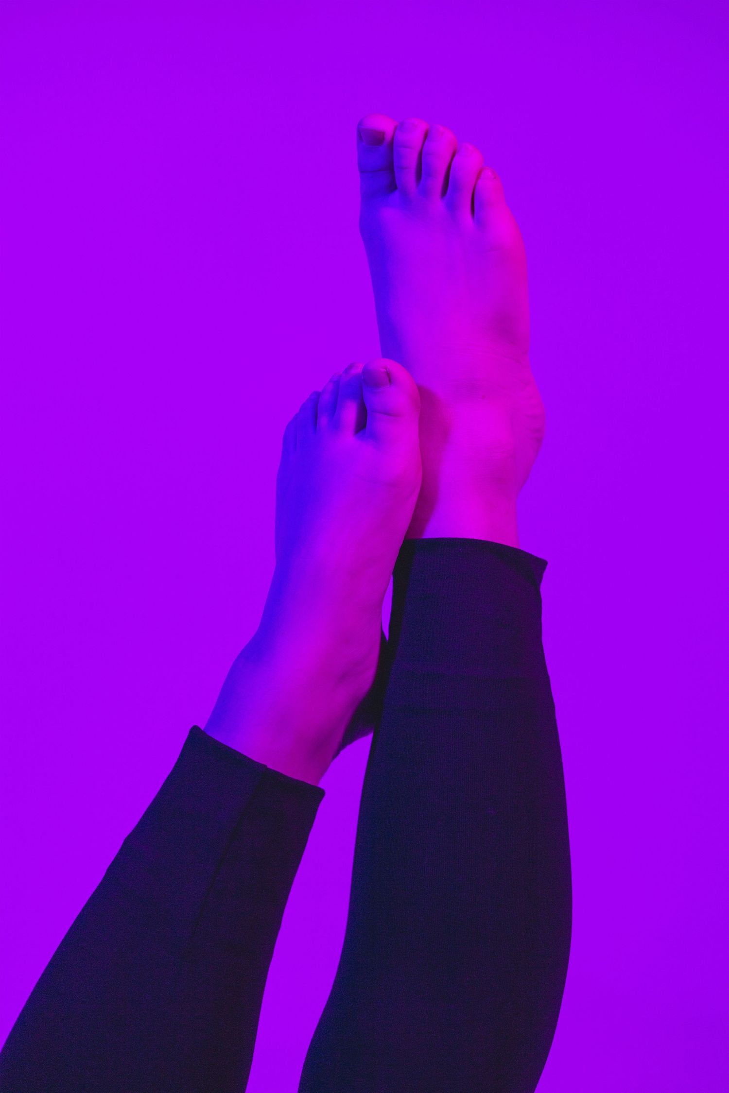 Bare feet against purple neon-lit background in artistic composition.