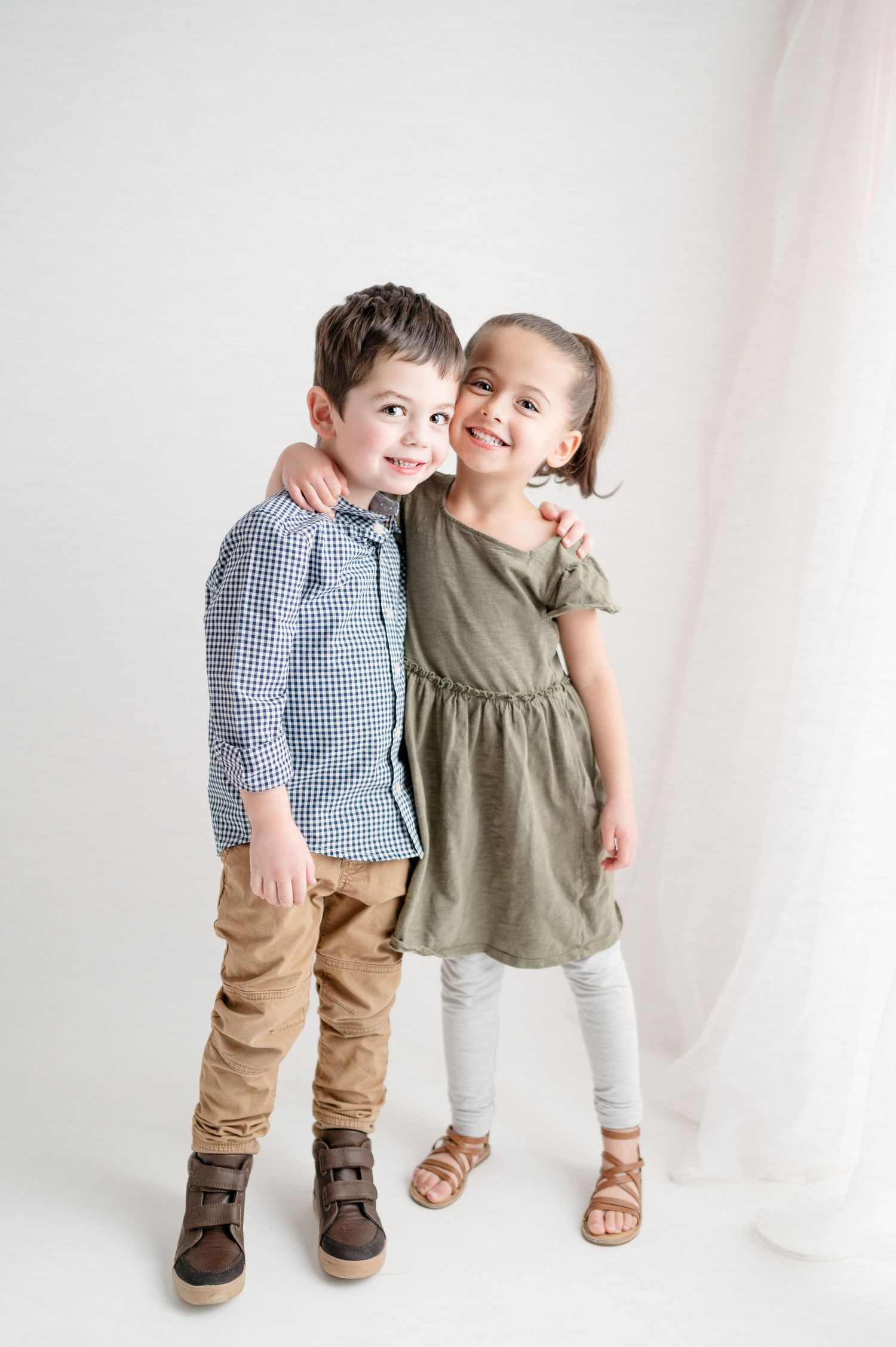 Two children in casual attire posing together against white background.