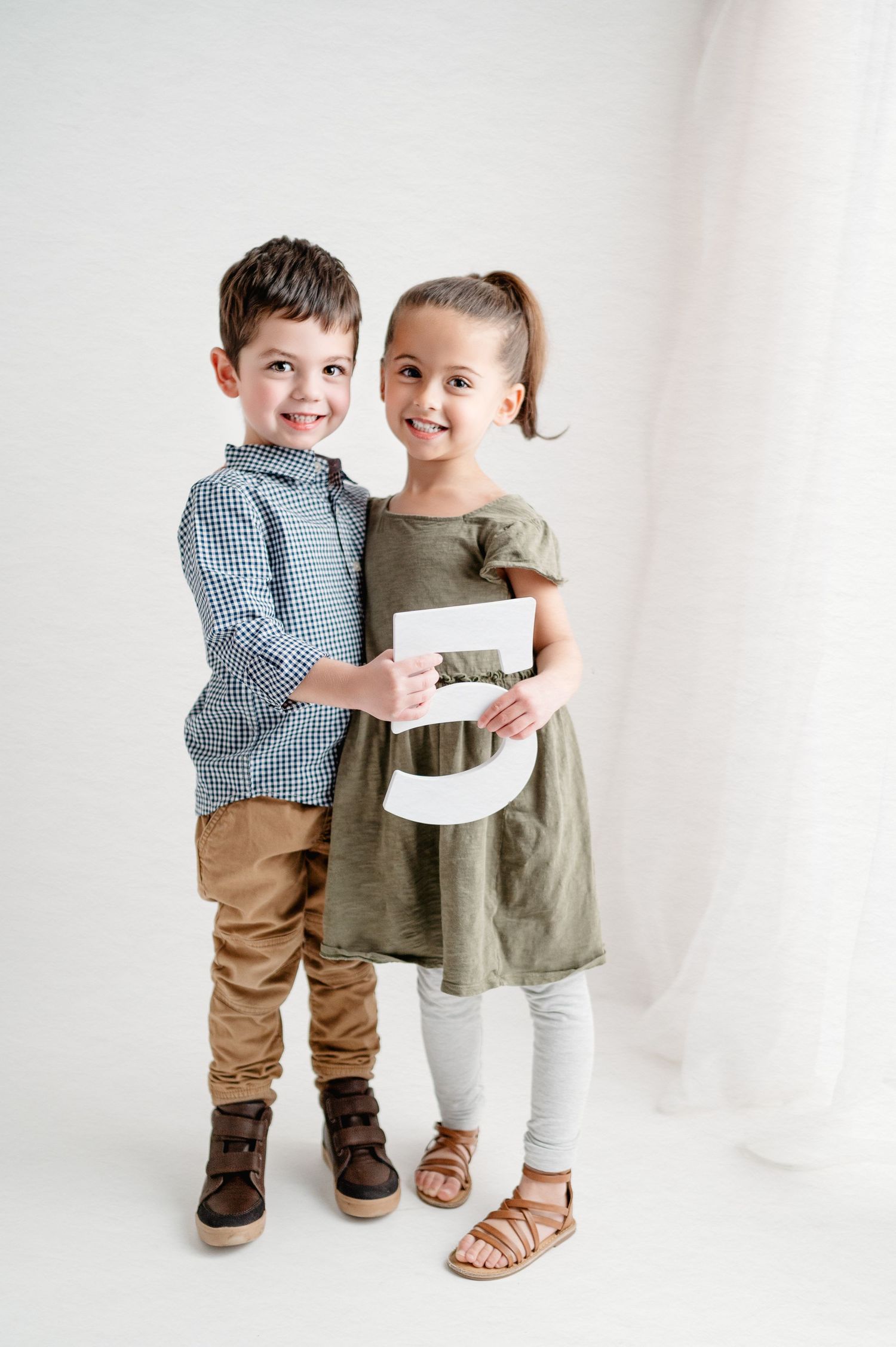 Two children in coordinated outfits holding letter together against white background.