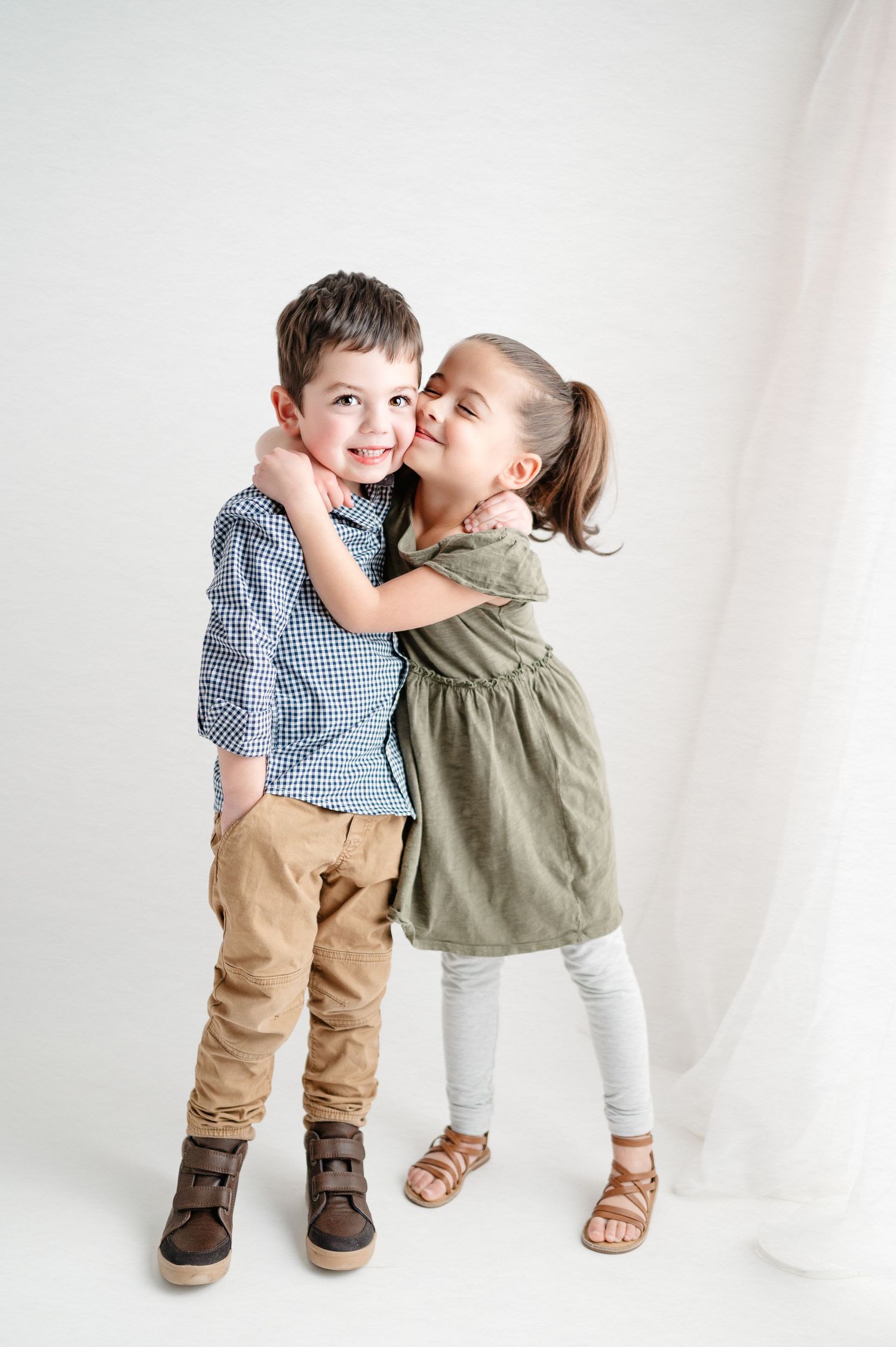 Candid moment of two children hugging and laughing against white backdrop.