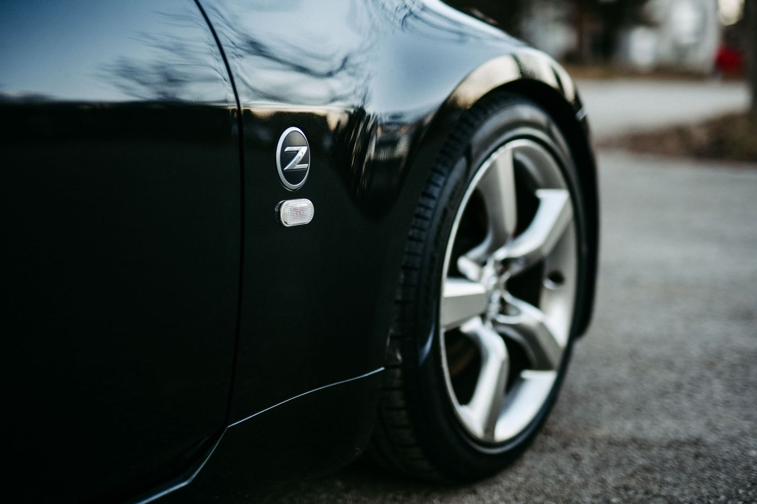 Close-up detail of black Nissan Z car wheel and fender badge.