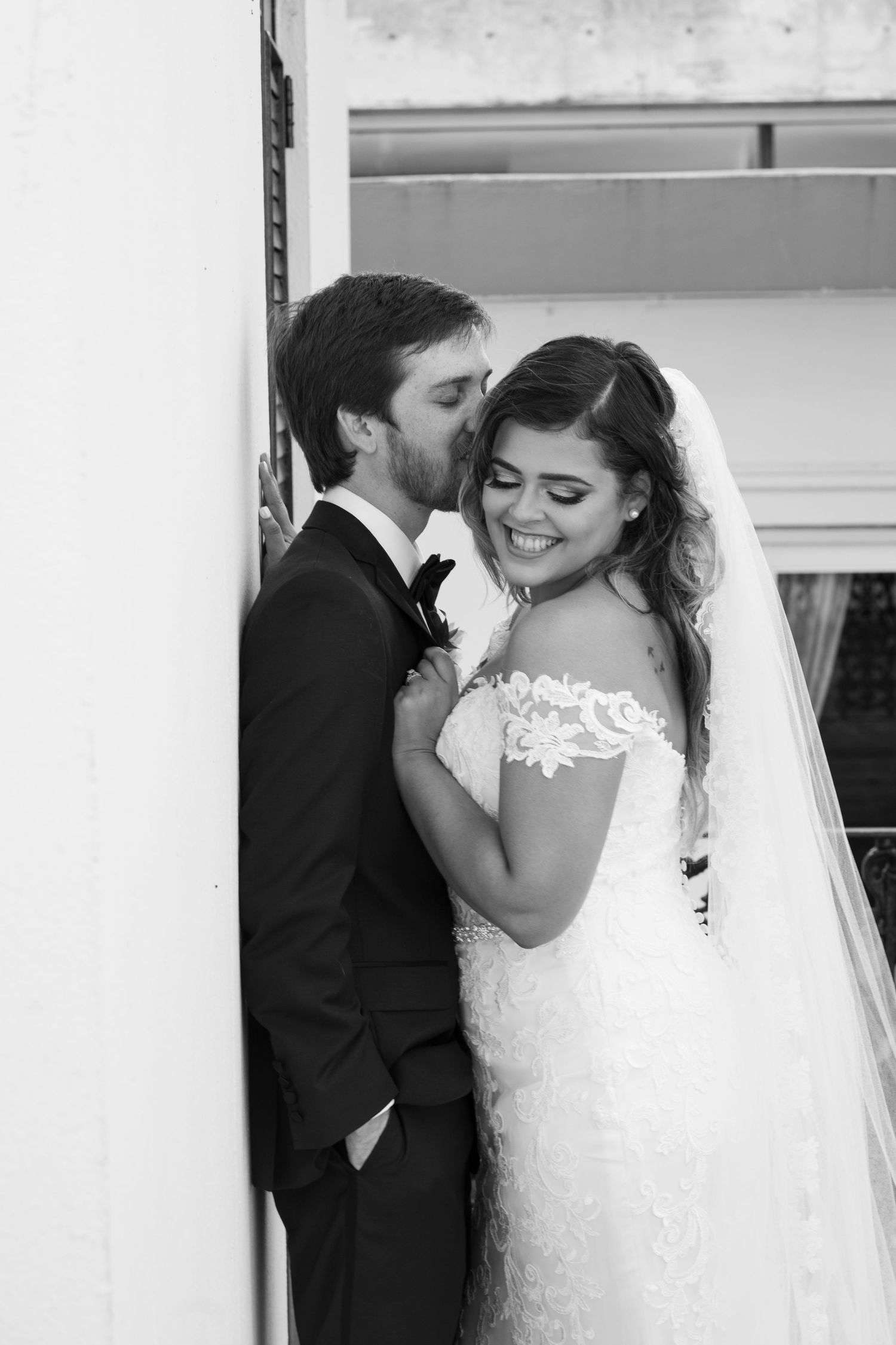 Black and white wedding photo of couple sharing intimate moment against wall.