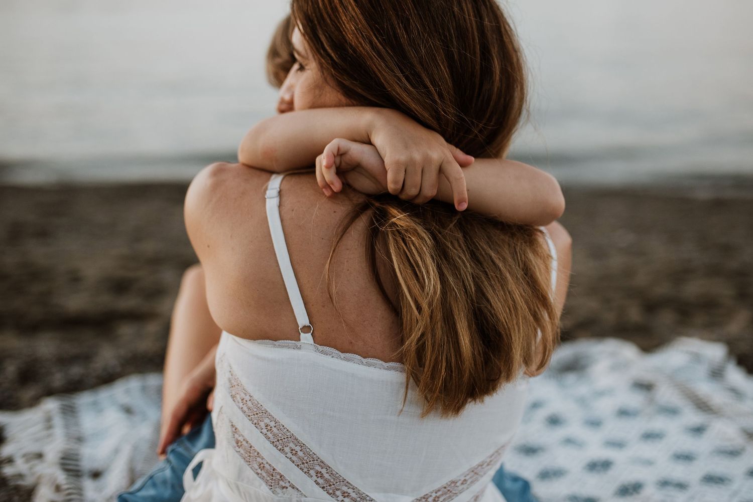 Close up of child arms around mother's neck with her long brown hair at the beach