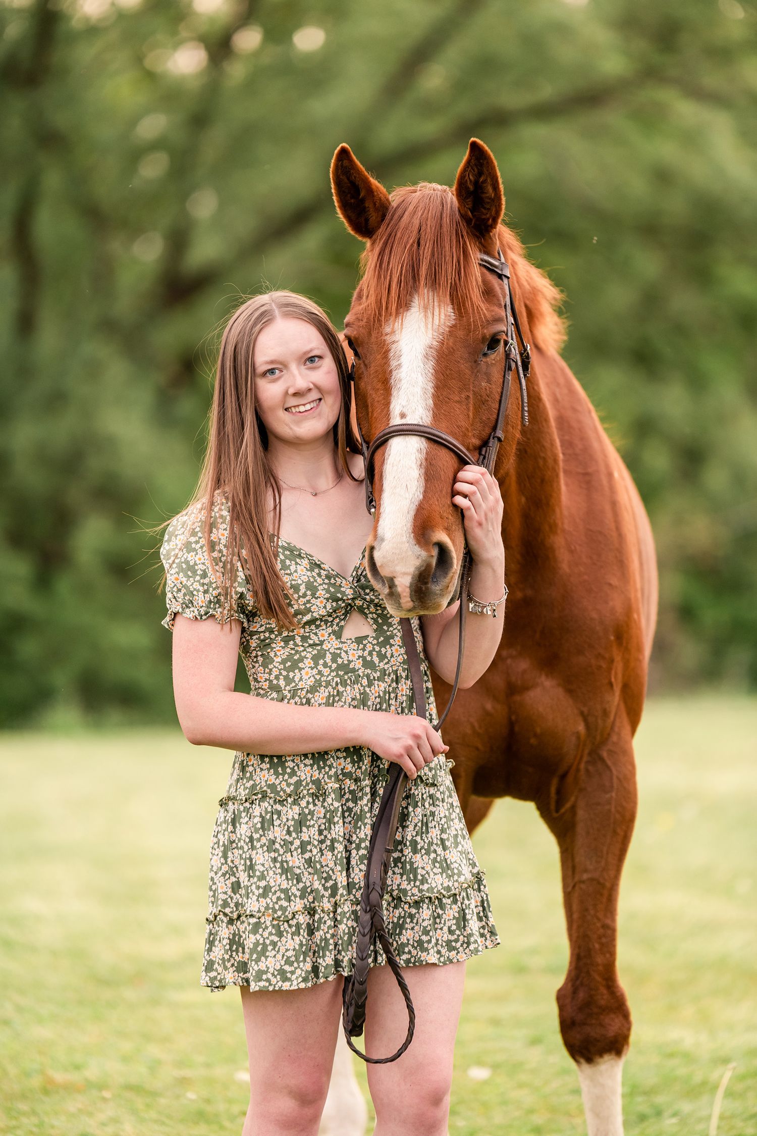 Girl in green floral dress with her arm around the nose of a chestnut Thoroughbred