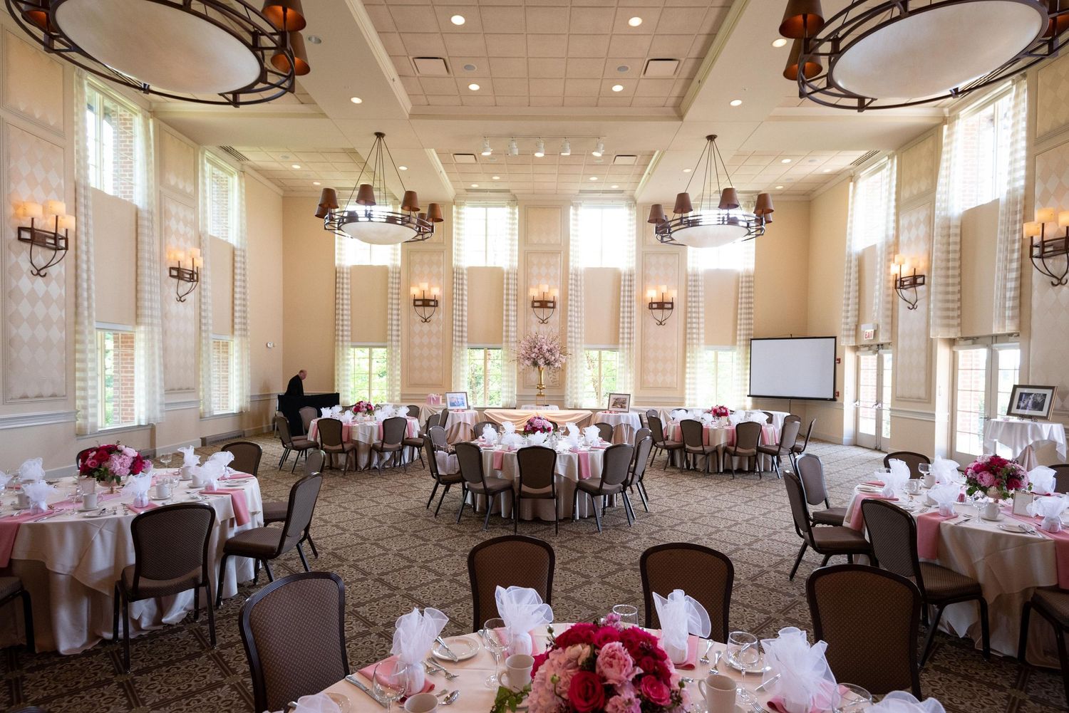 Elegant ballroom with round tables and pink decor set for a formal wedding reception.
