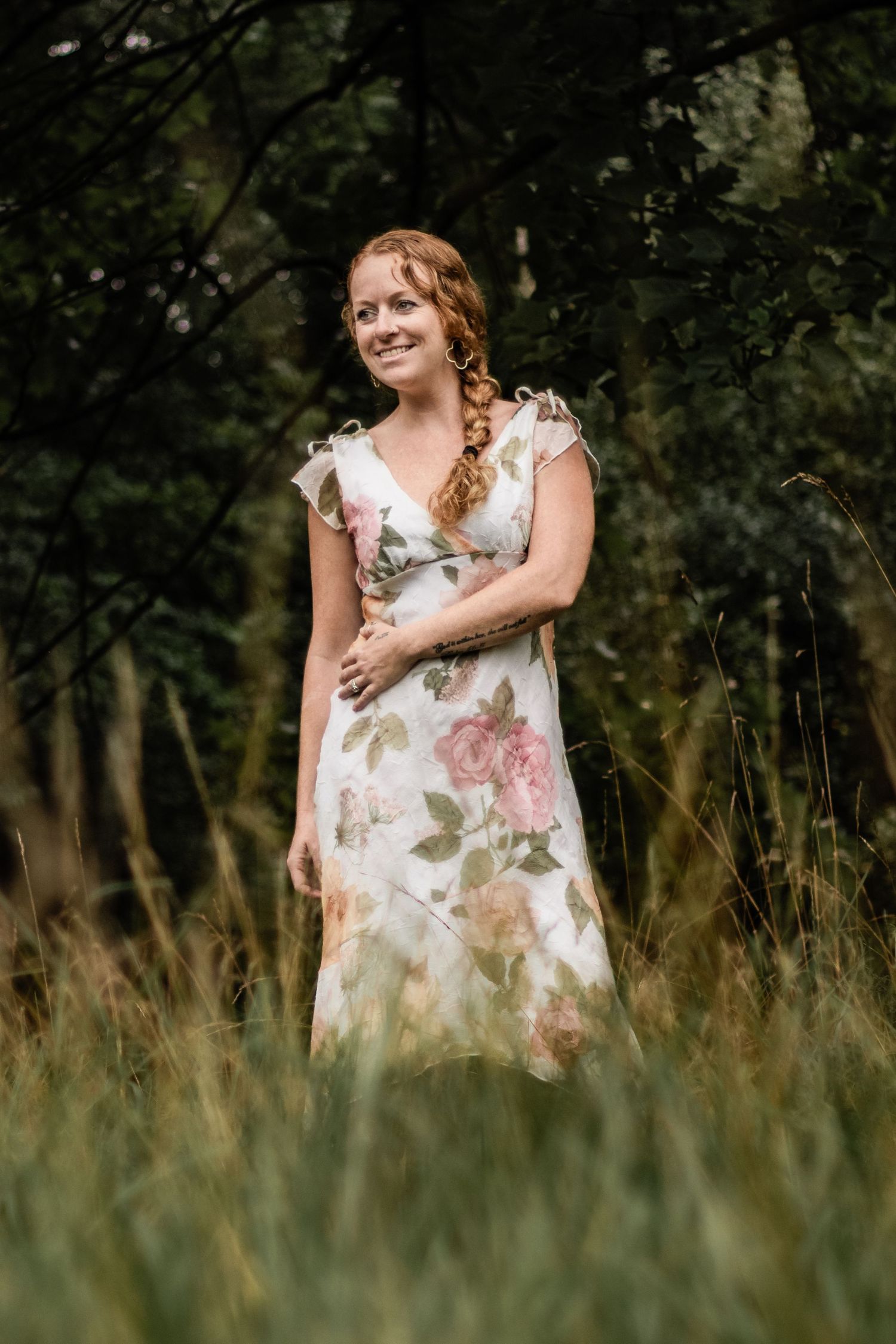 Person in floral dress poses in tall grass with natural lighting.