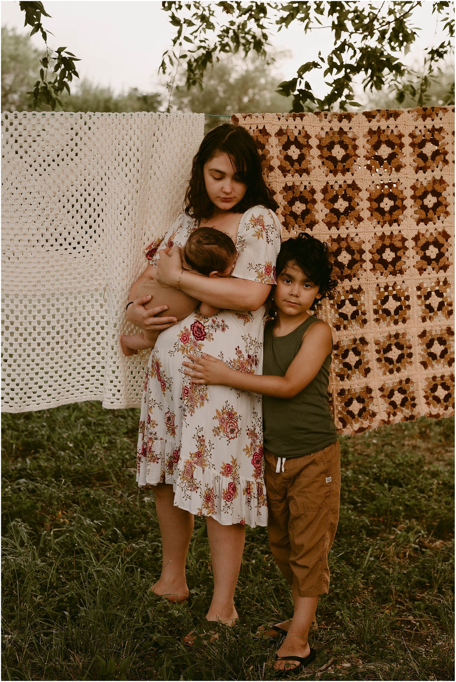 A tender family moment outdoors with a patterned quilt backdrop in warm sunset lighting.