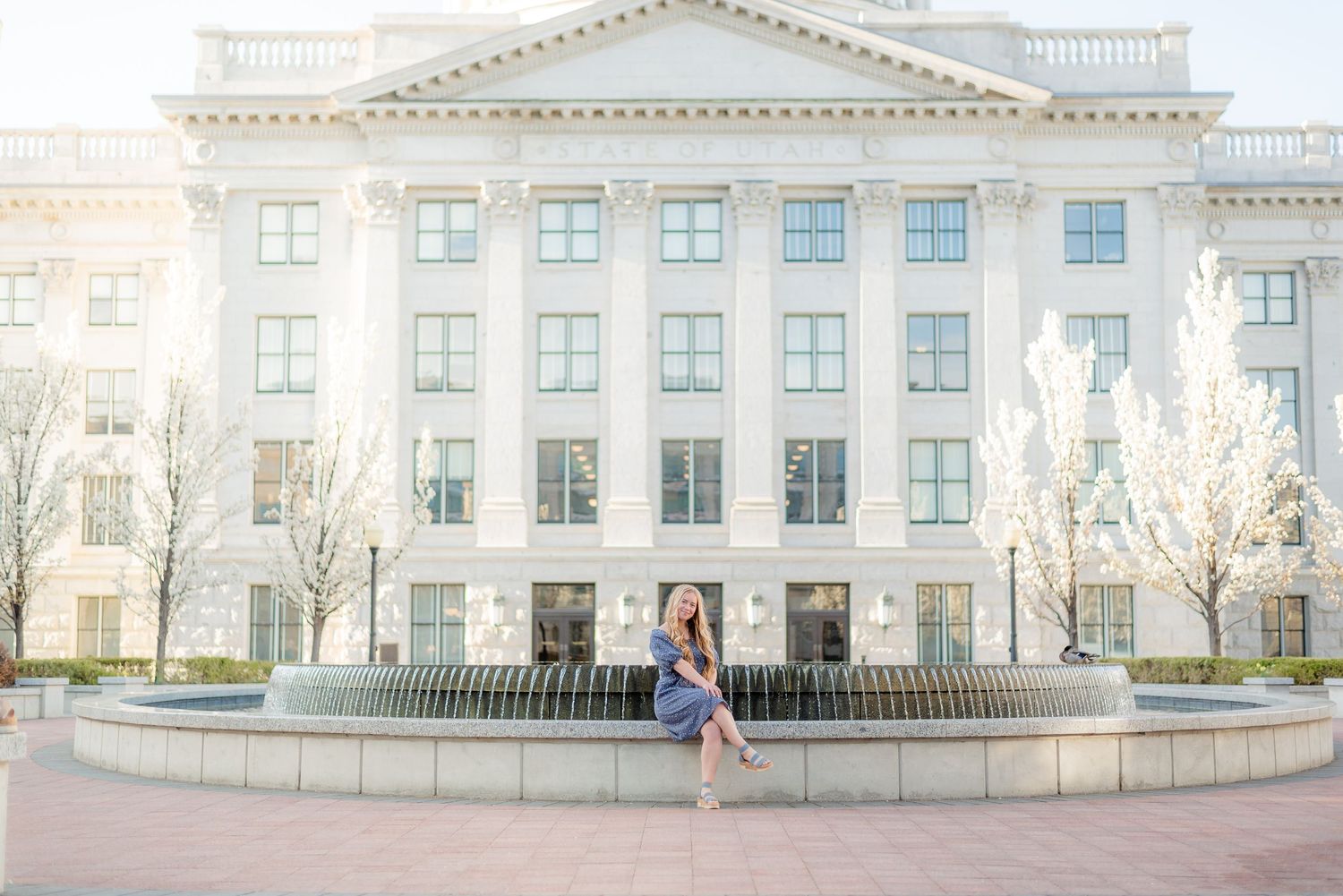 Senior girl in blue dress posing by fountain in front of large white neoclassical building. Megan Snell Photo Utah Weddings