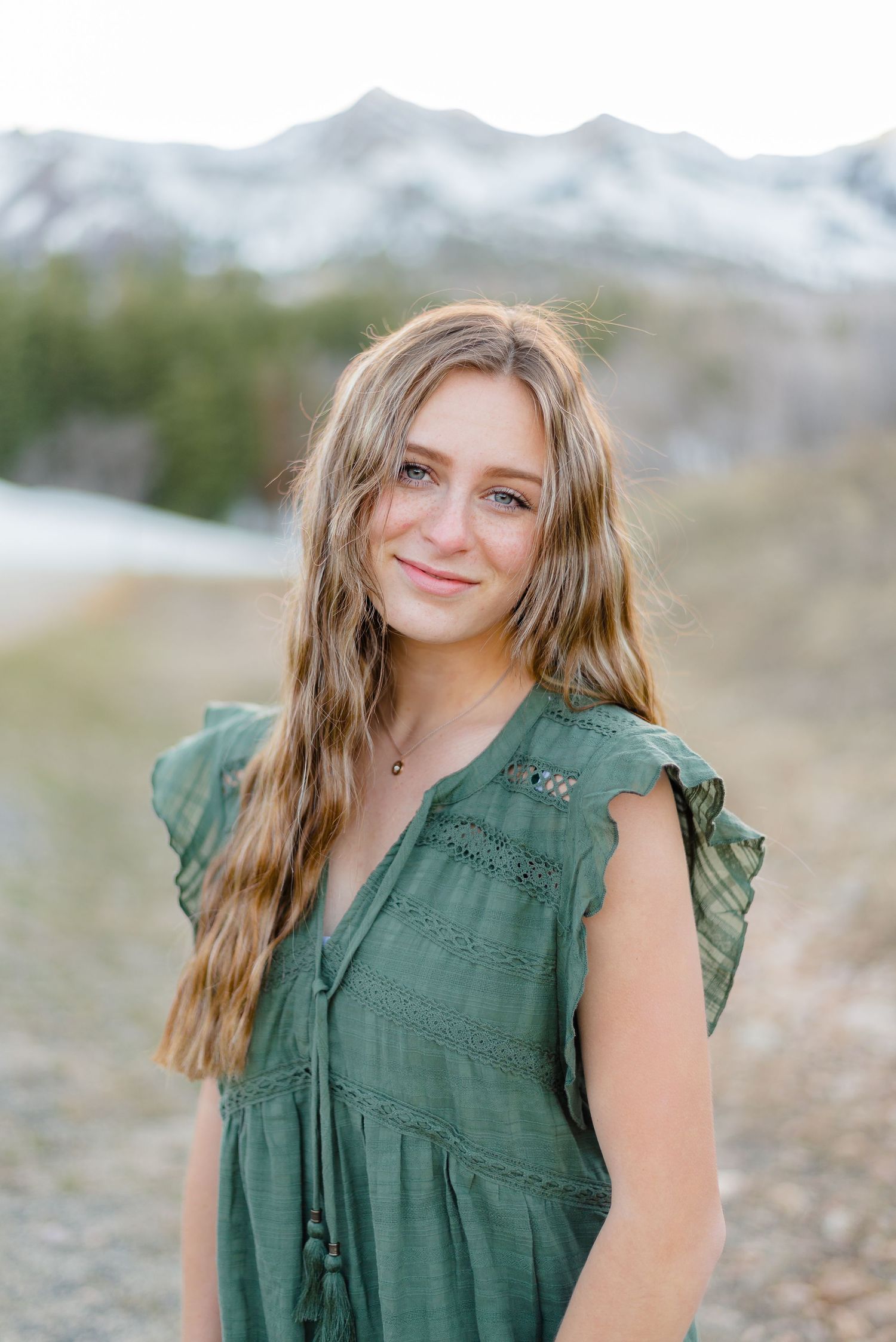 Smiling teenage girl in green dress with snowy mountains and rocky terrain in the background. Megan Snell Photo Utah Weddings