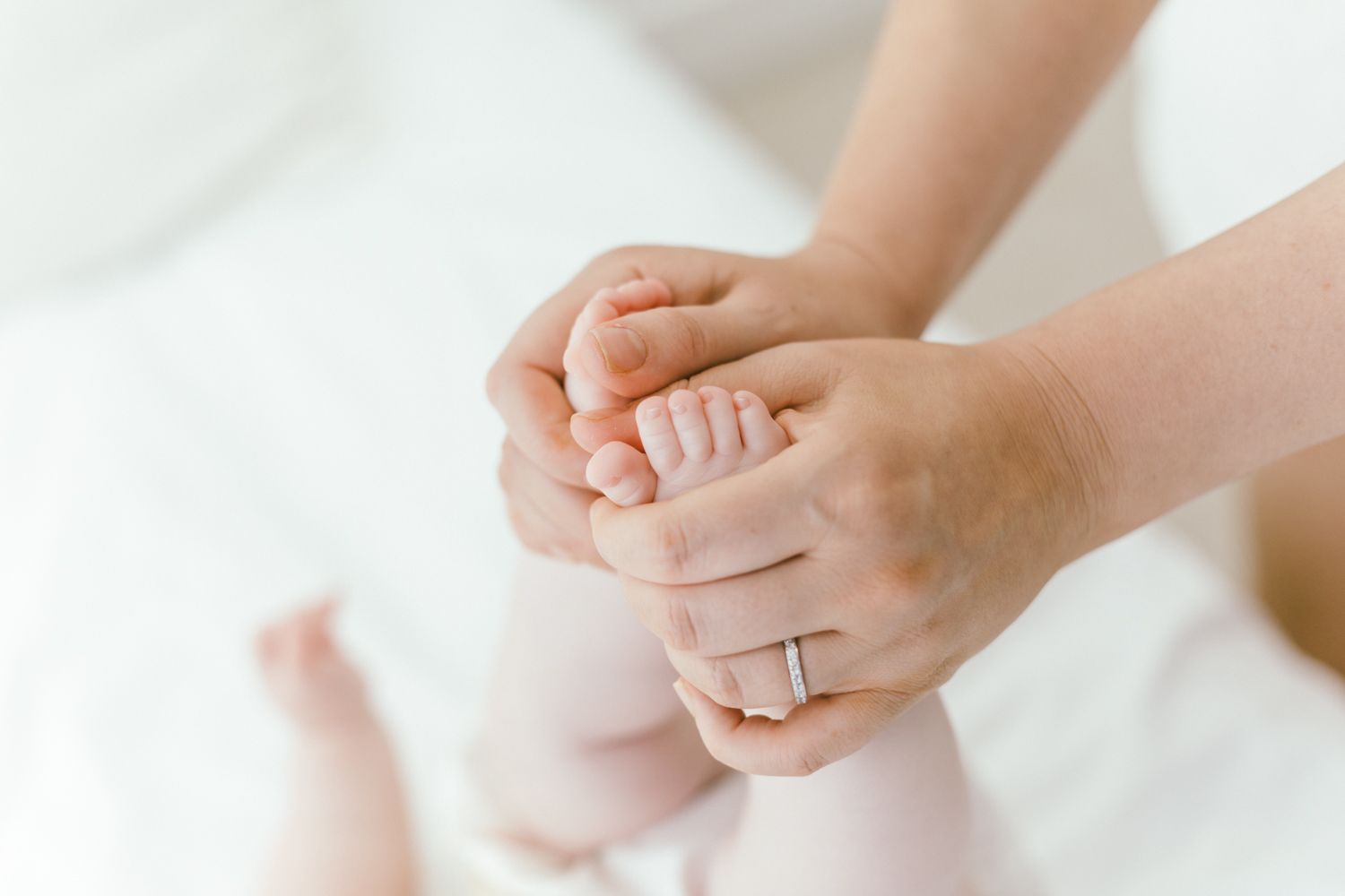 Gentle hands holding tiny baby feet against white background.
